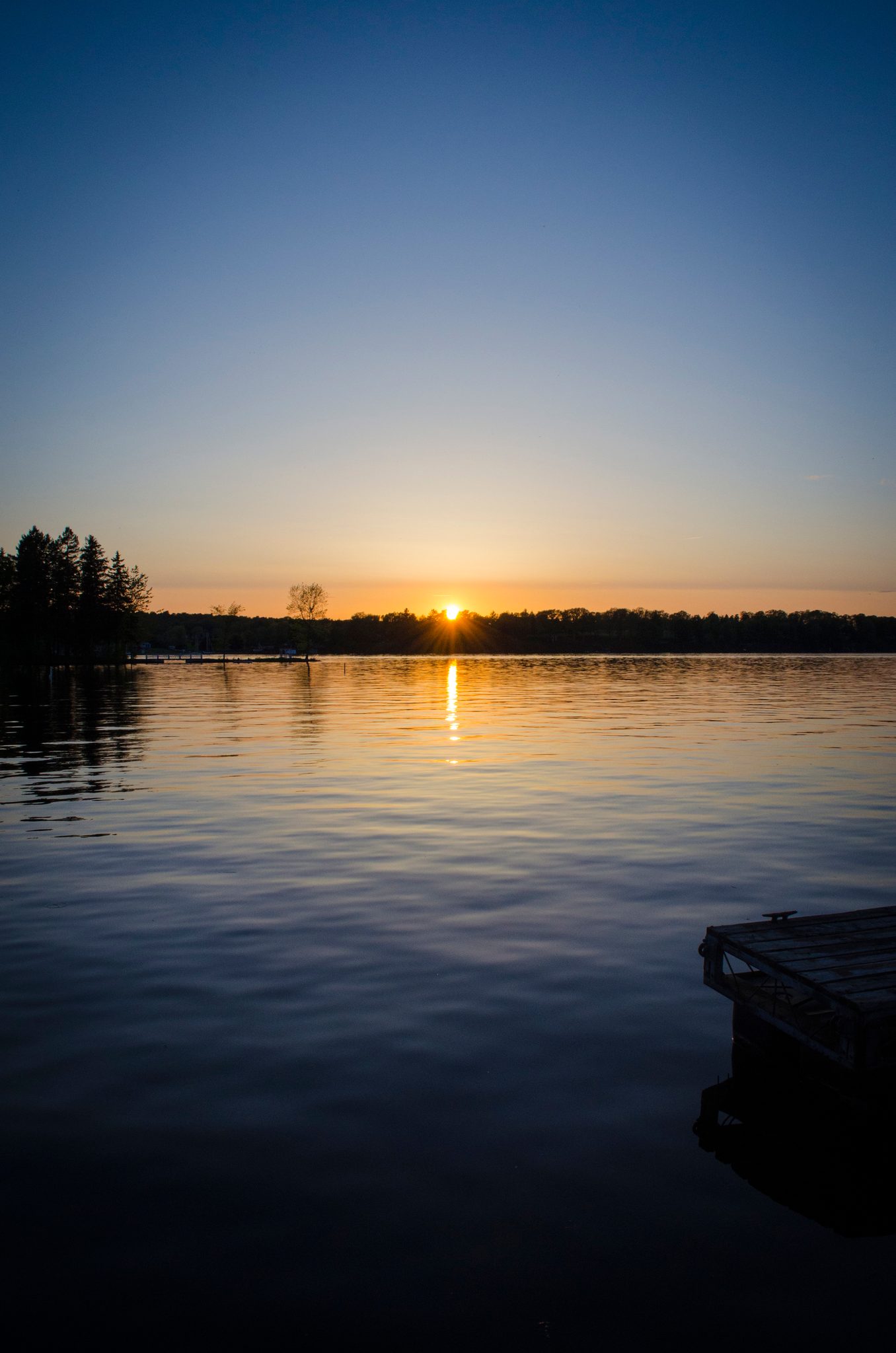 A dock half-hidden in the dark water as the sun sinks into the bay.