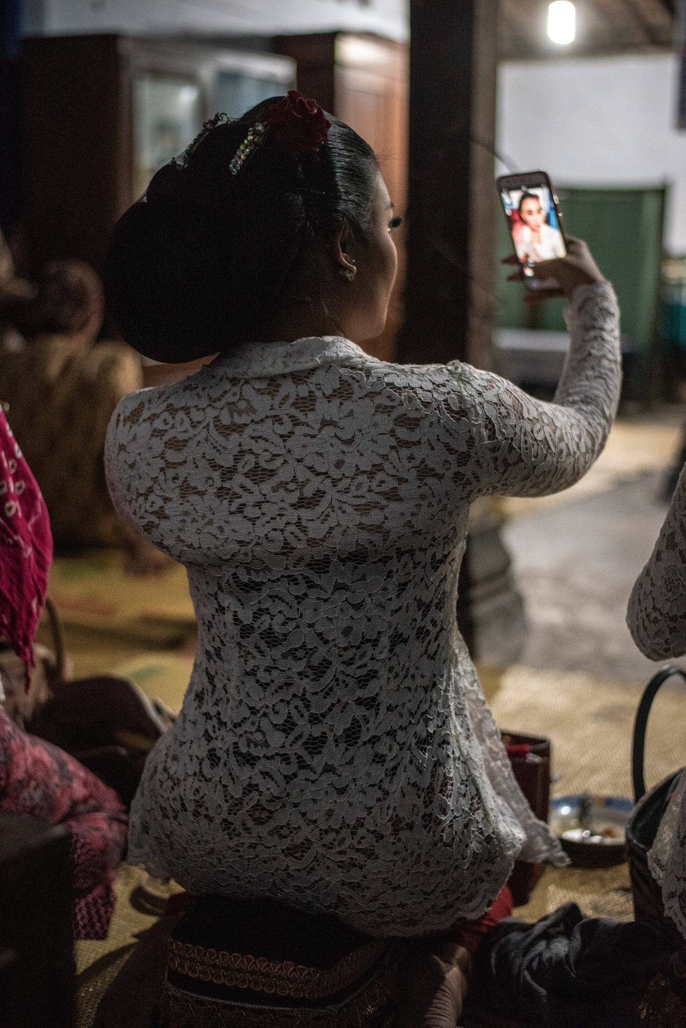 A singer in white lace checks her makeup in her phone's camera.