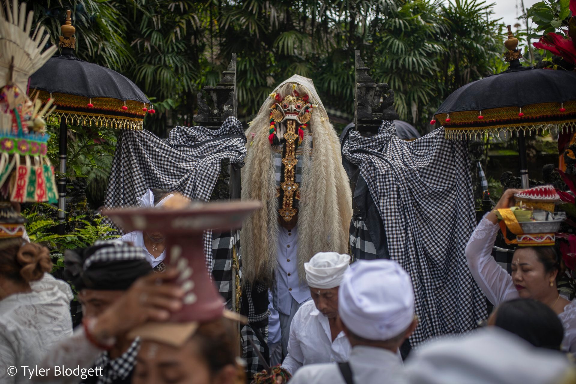 Between shrines draped in checked cloth, the figure waits while offerings pass overhead.