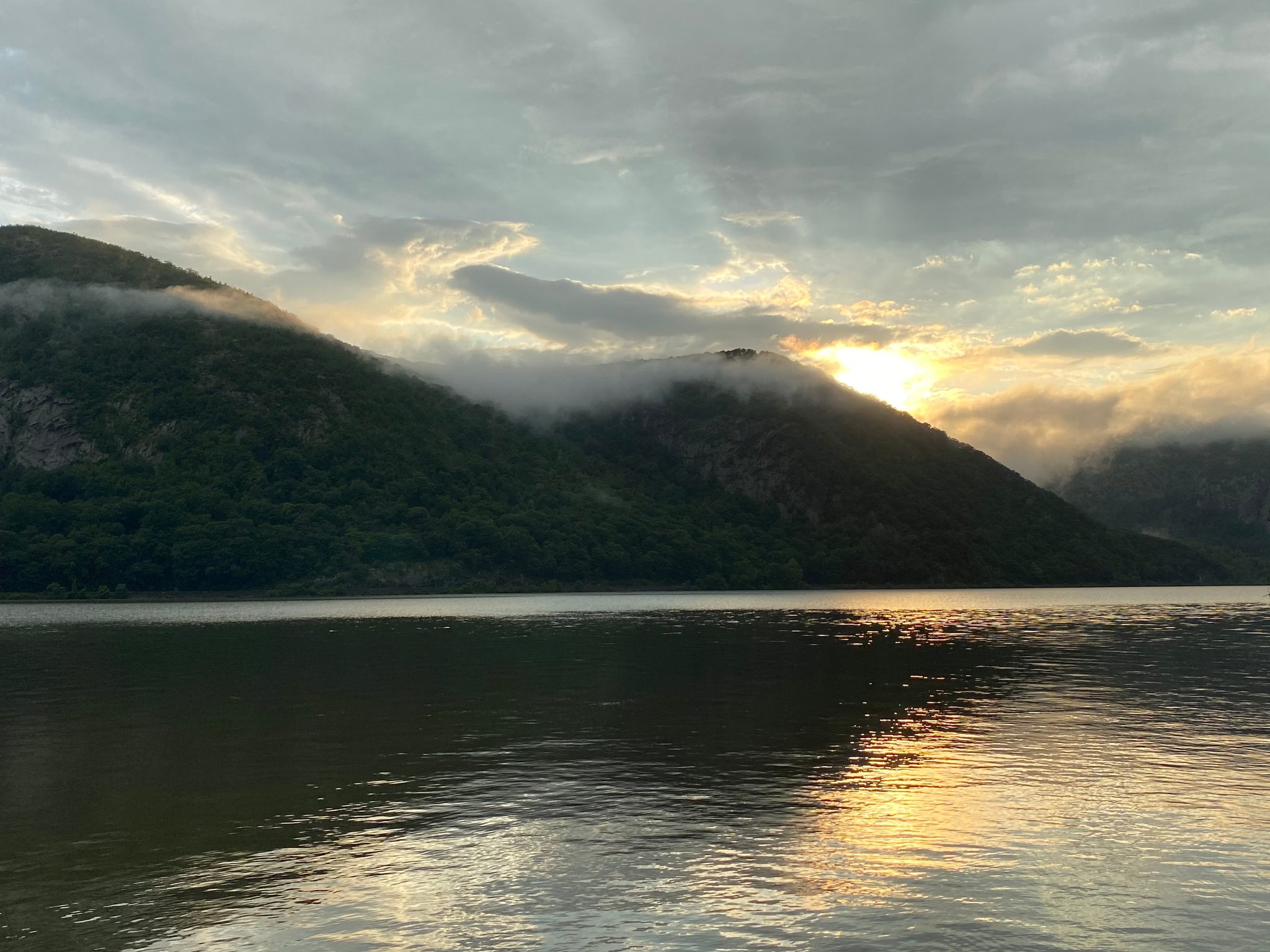 A gold sun breaks through over the misty ridge, doubled in the river.