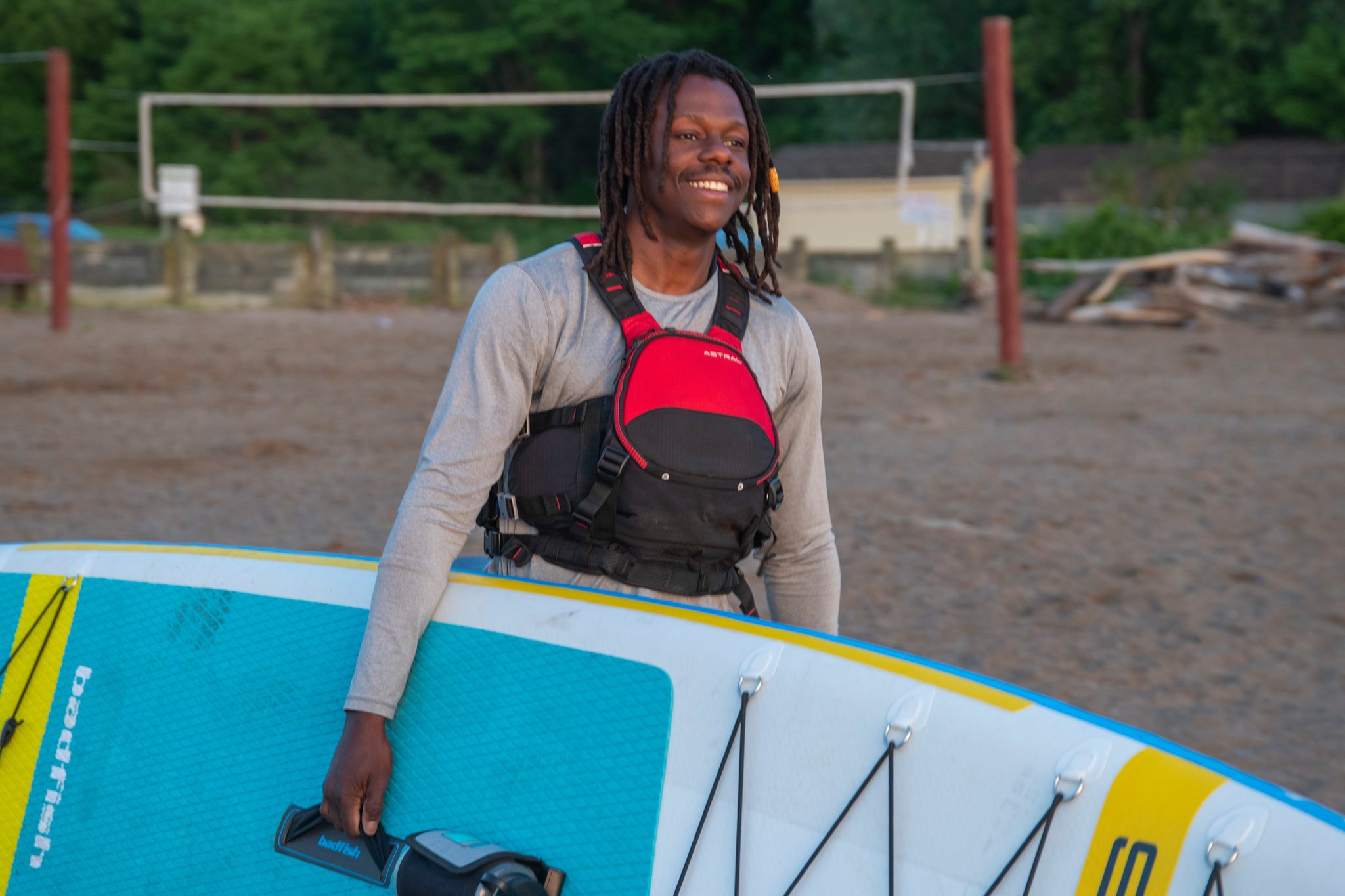Chev breaks into a laugh with the inflated board propped against him on the beach.