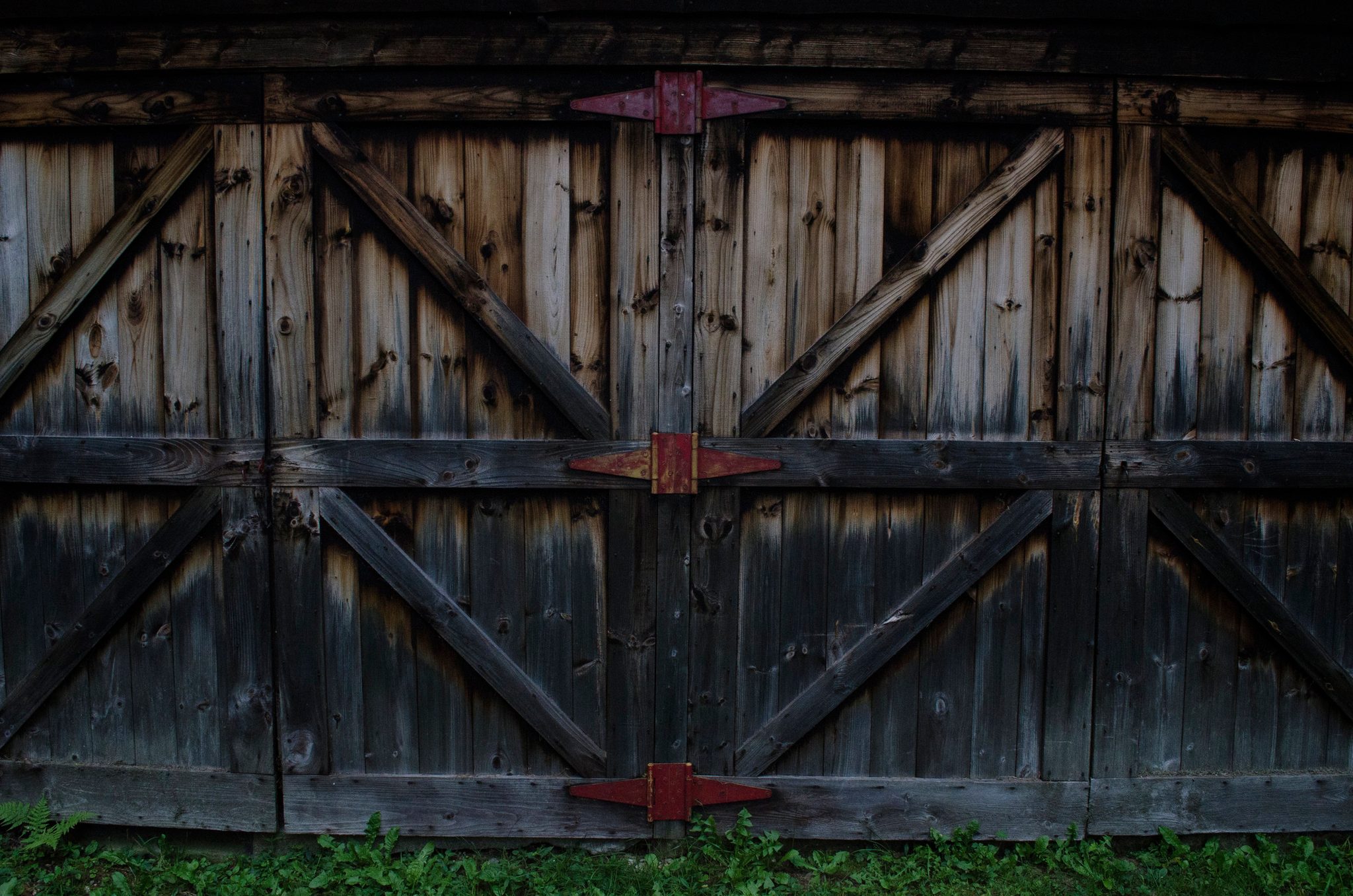 Weathered barn doors held shut with red iron hinges.