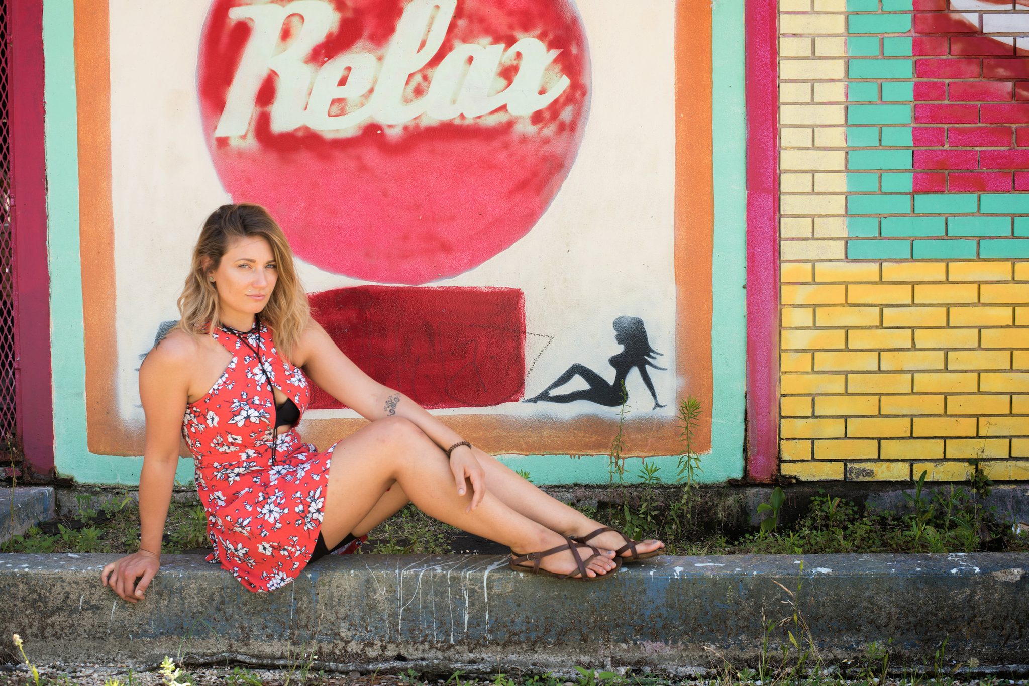 A woman in red rests on the curb beneath a mural that says Relax.