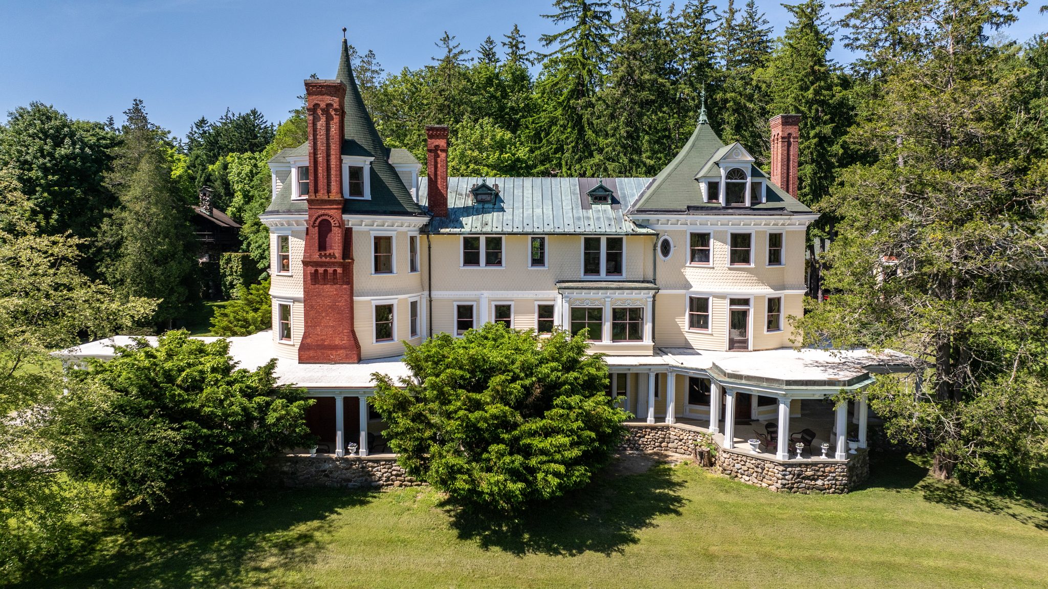 Shingled walls, green slate turrets and a tall red brick chimney, with the wraparound porch resting on a fieldstone base.