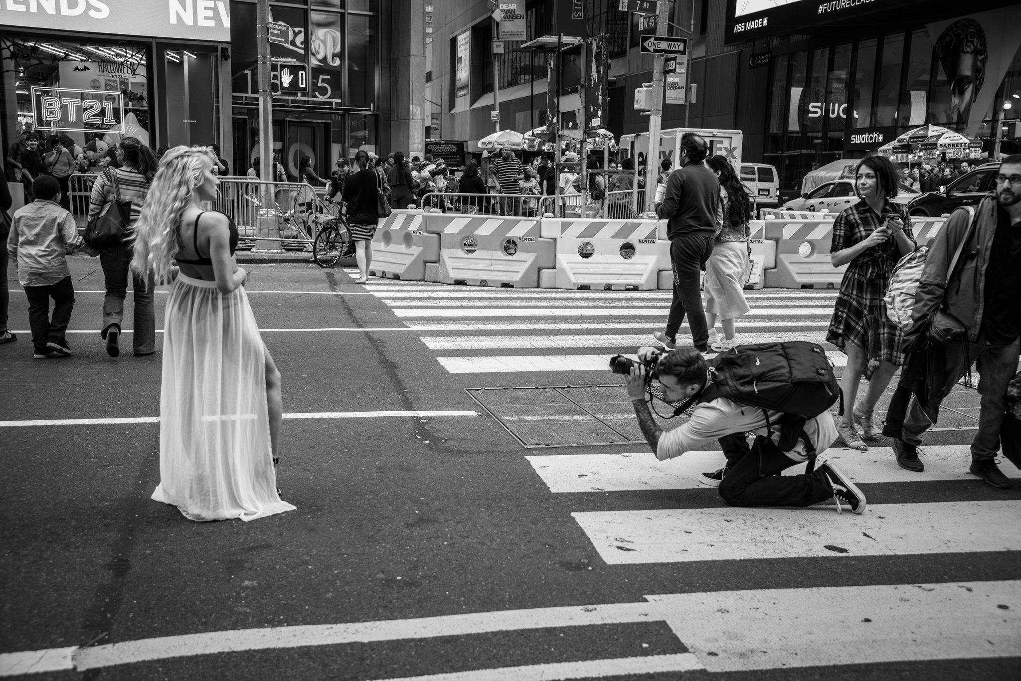 A model in a flowing gown holds her pose in the crosswalk while the photographer drops to one knee.