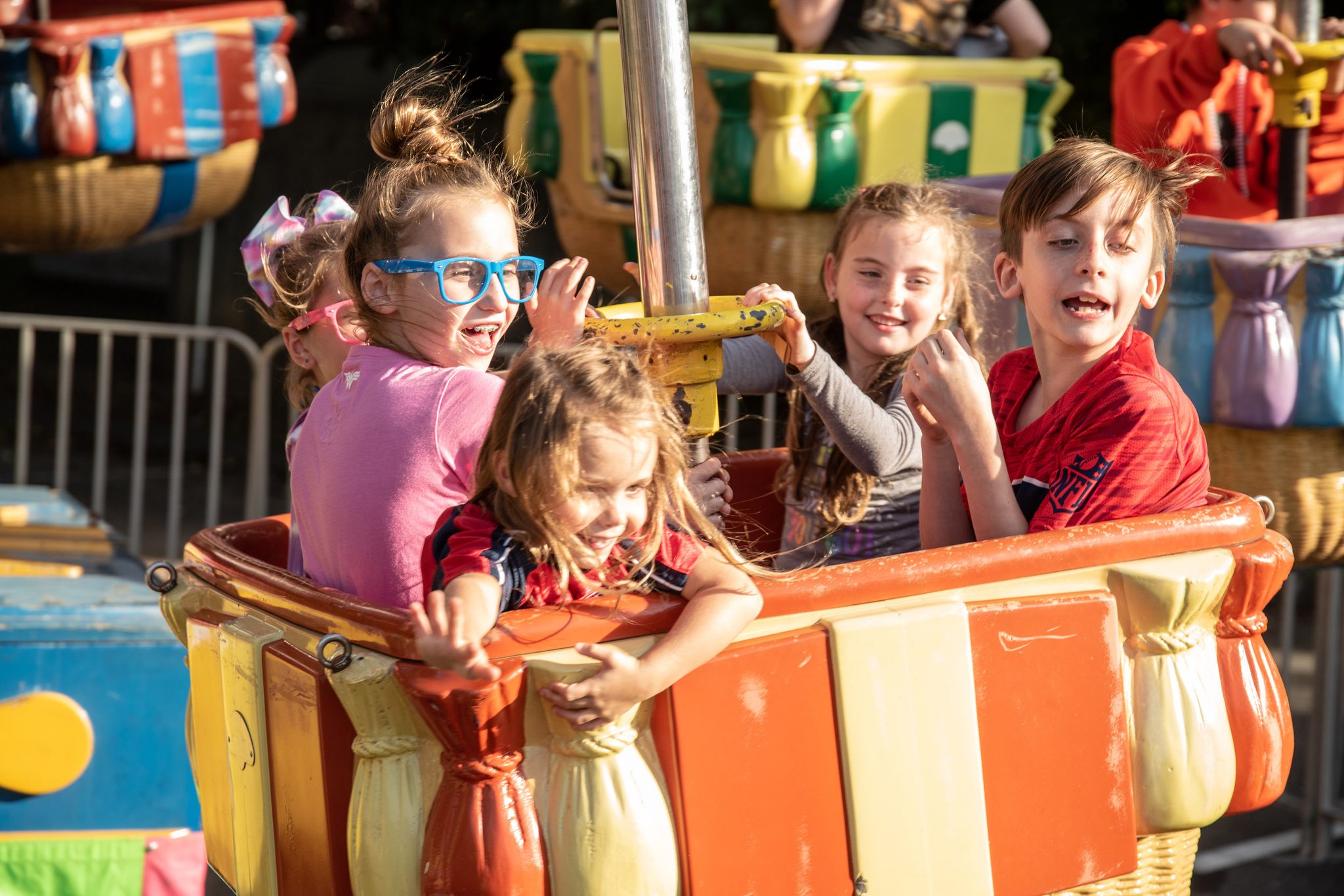 Kids squeal on the spinning teacups, one pair of blue glasses bravely holding on.