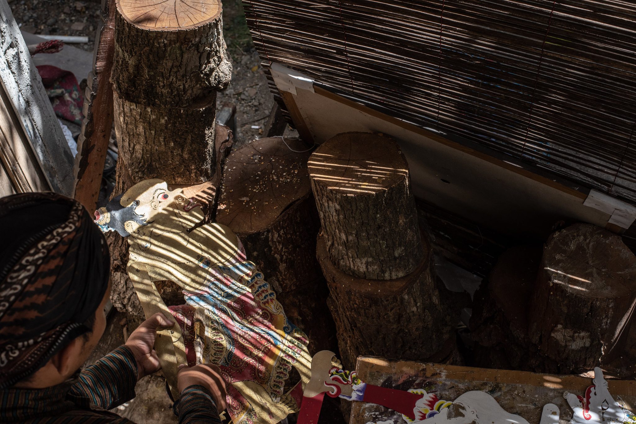 Sunlight through the bamboo blind stripes the puppets as he sorts them.