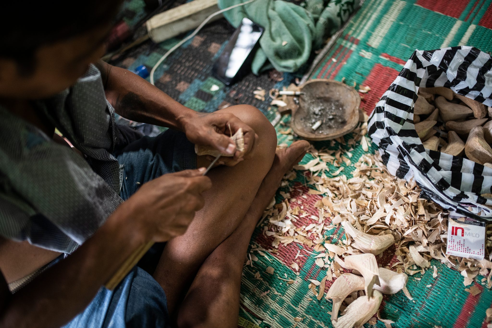 Wood shavings pile up as a carver works a blade into a small figure.