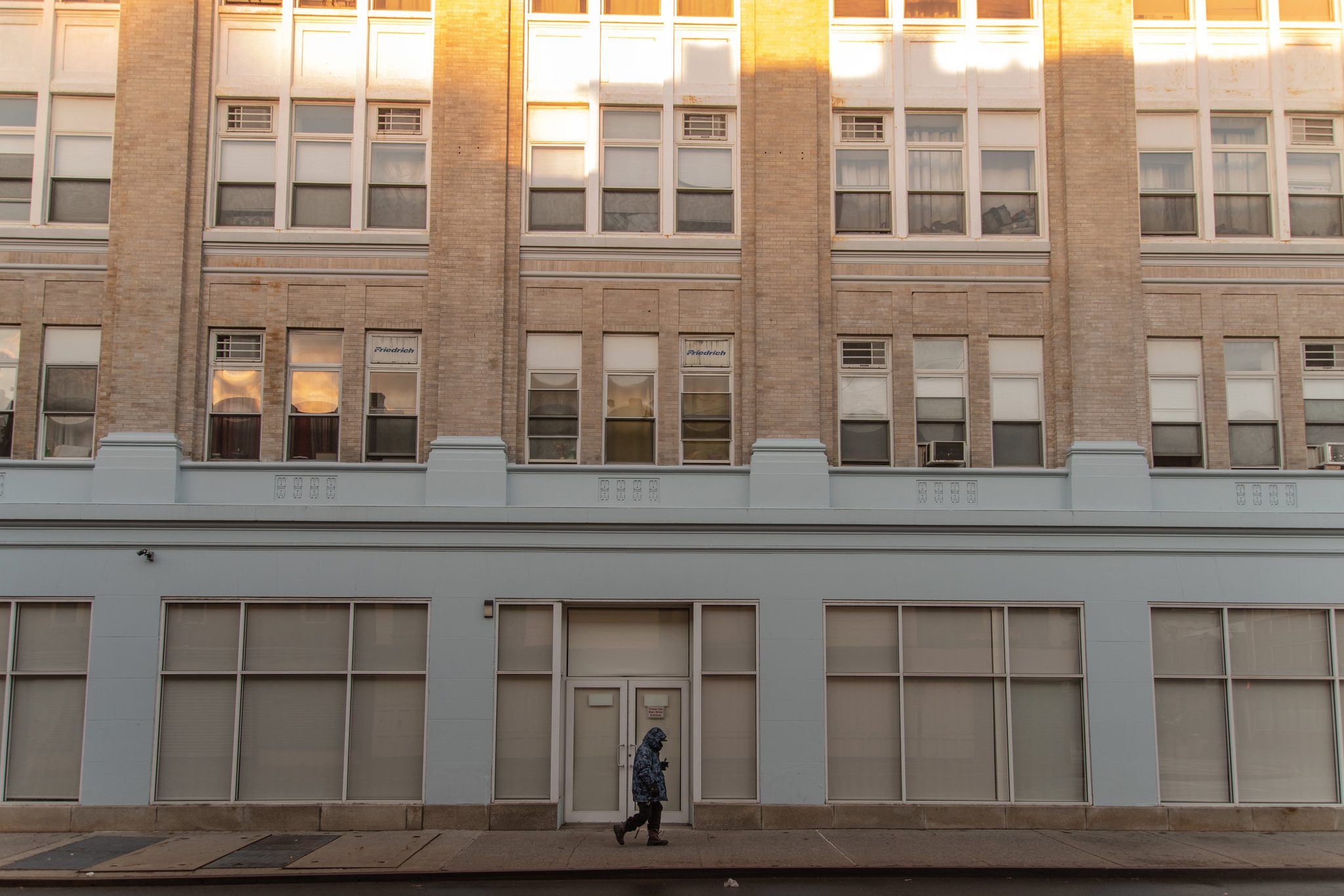 A lone walker passes beneath the tall windows of an old downtown building.