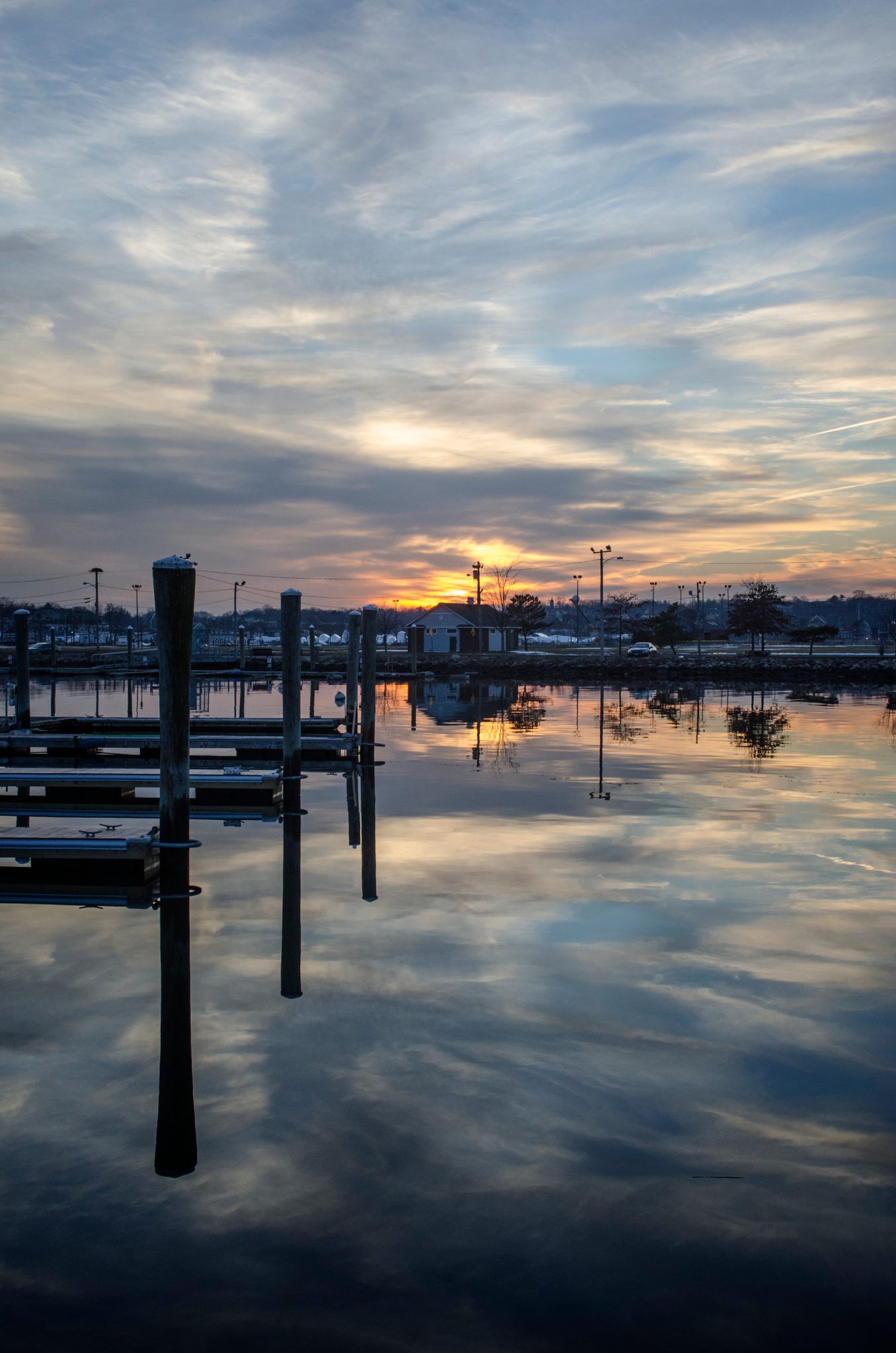 Dock pilings stand in the water as the sunset clouds spread across it.