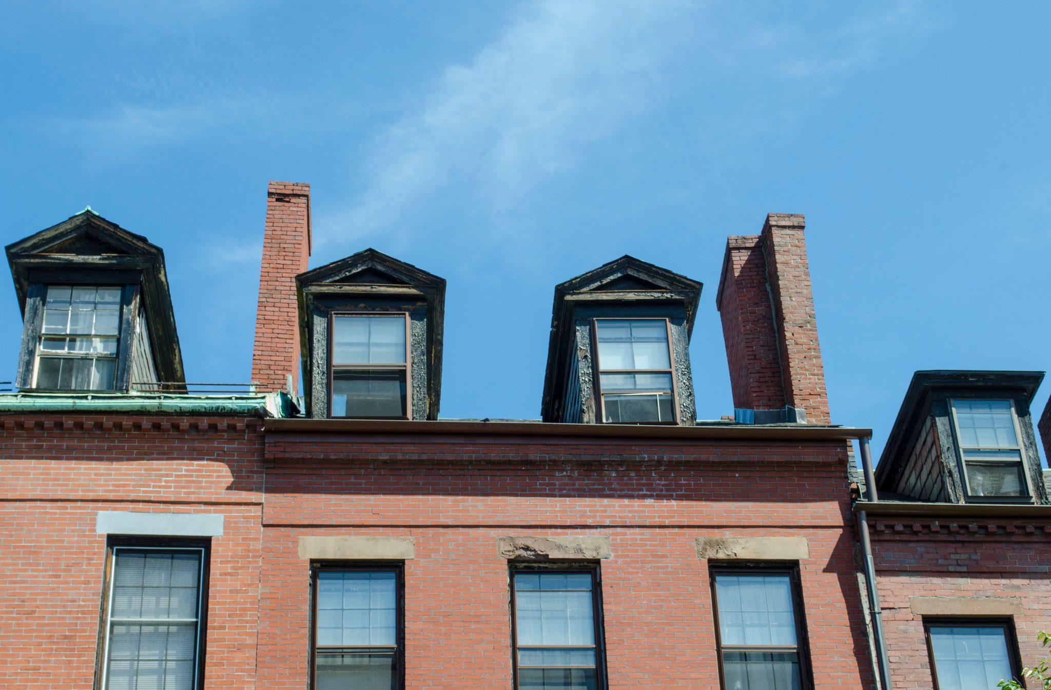 Dormer windows line up along the roof of a brick row house.