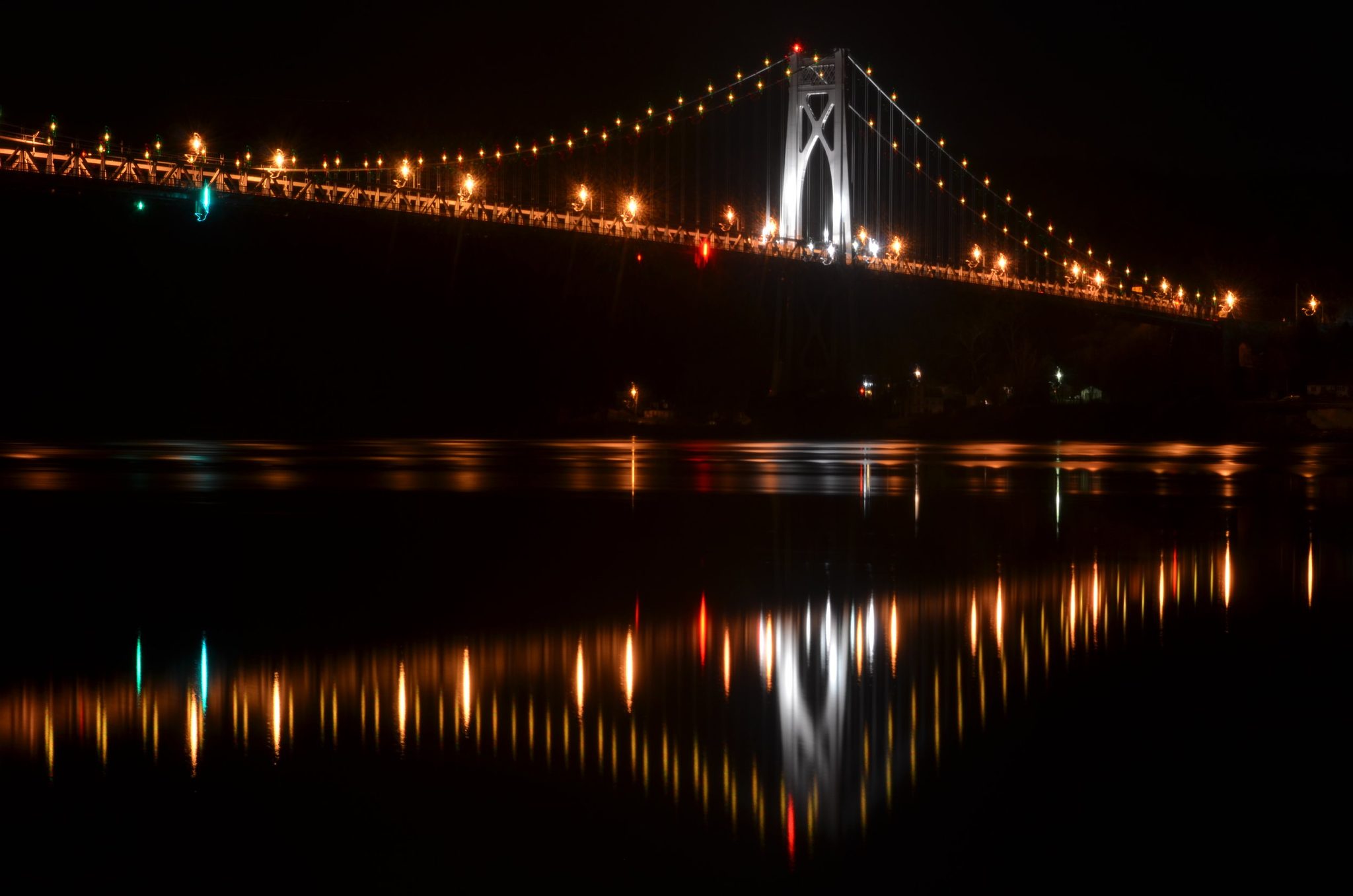 The Mid-Hudson Bridge glows in a string of lights across the night river.
