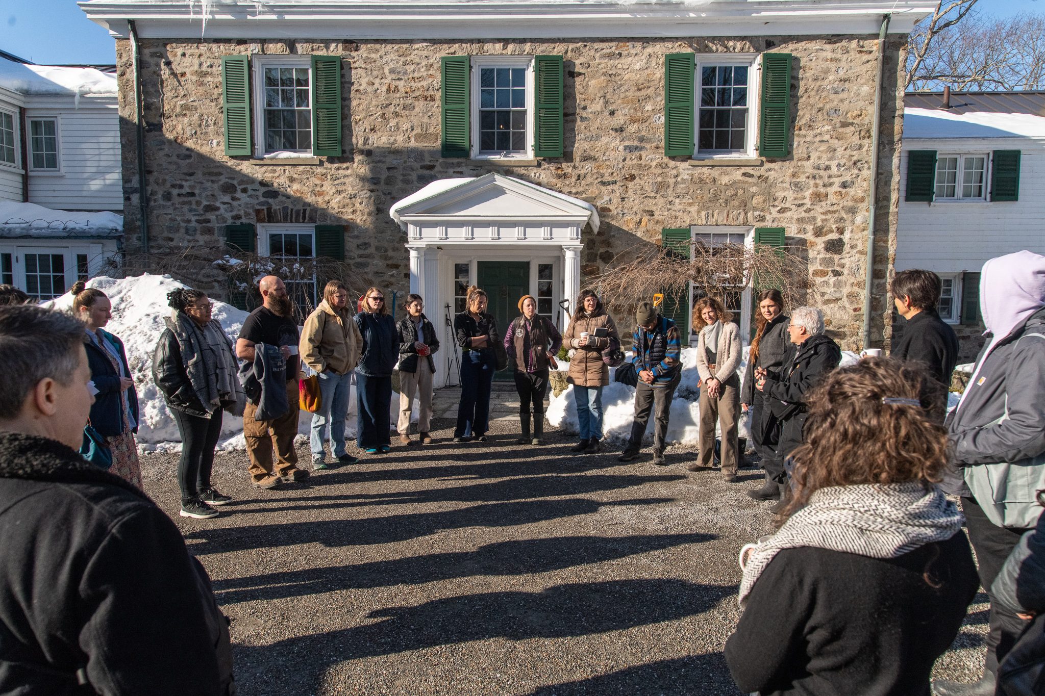 The group circles up outside the stone house in the morning sun.