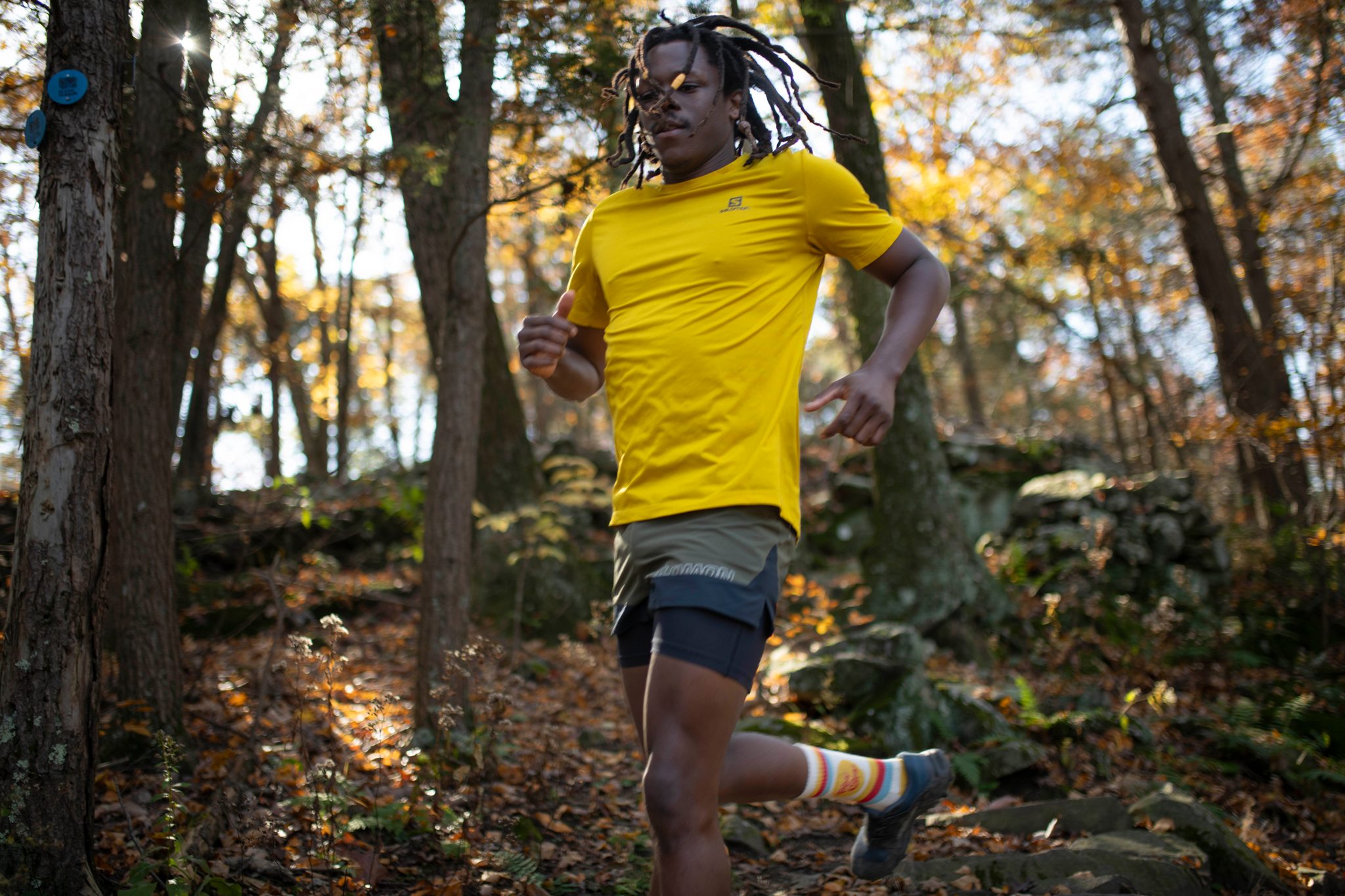 Sun flares through the trees as he runs straight at the lens.