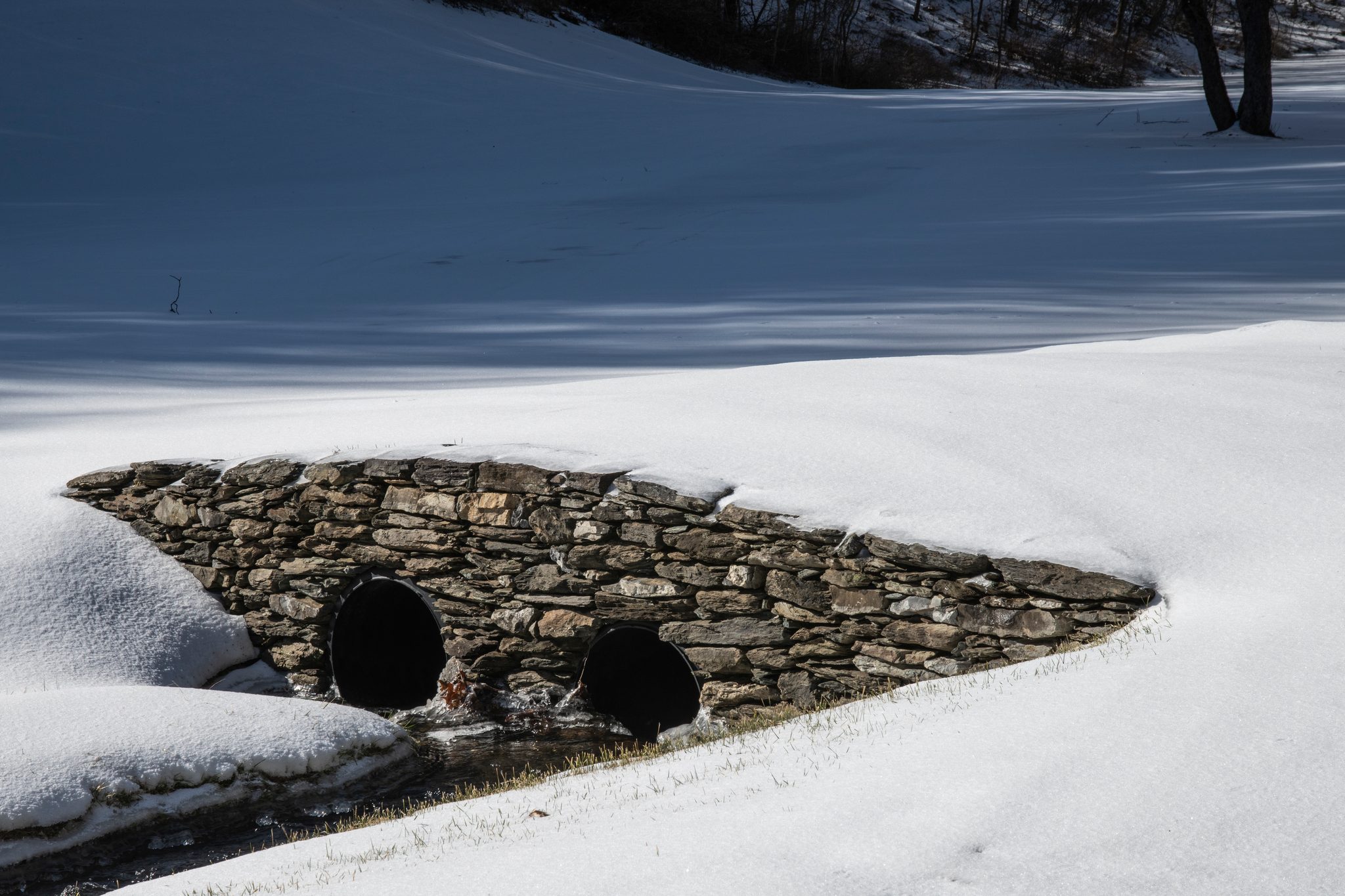 A stone culvert carries the stream under a drift of snow.