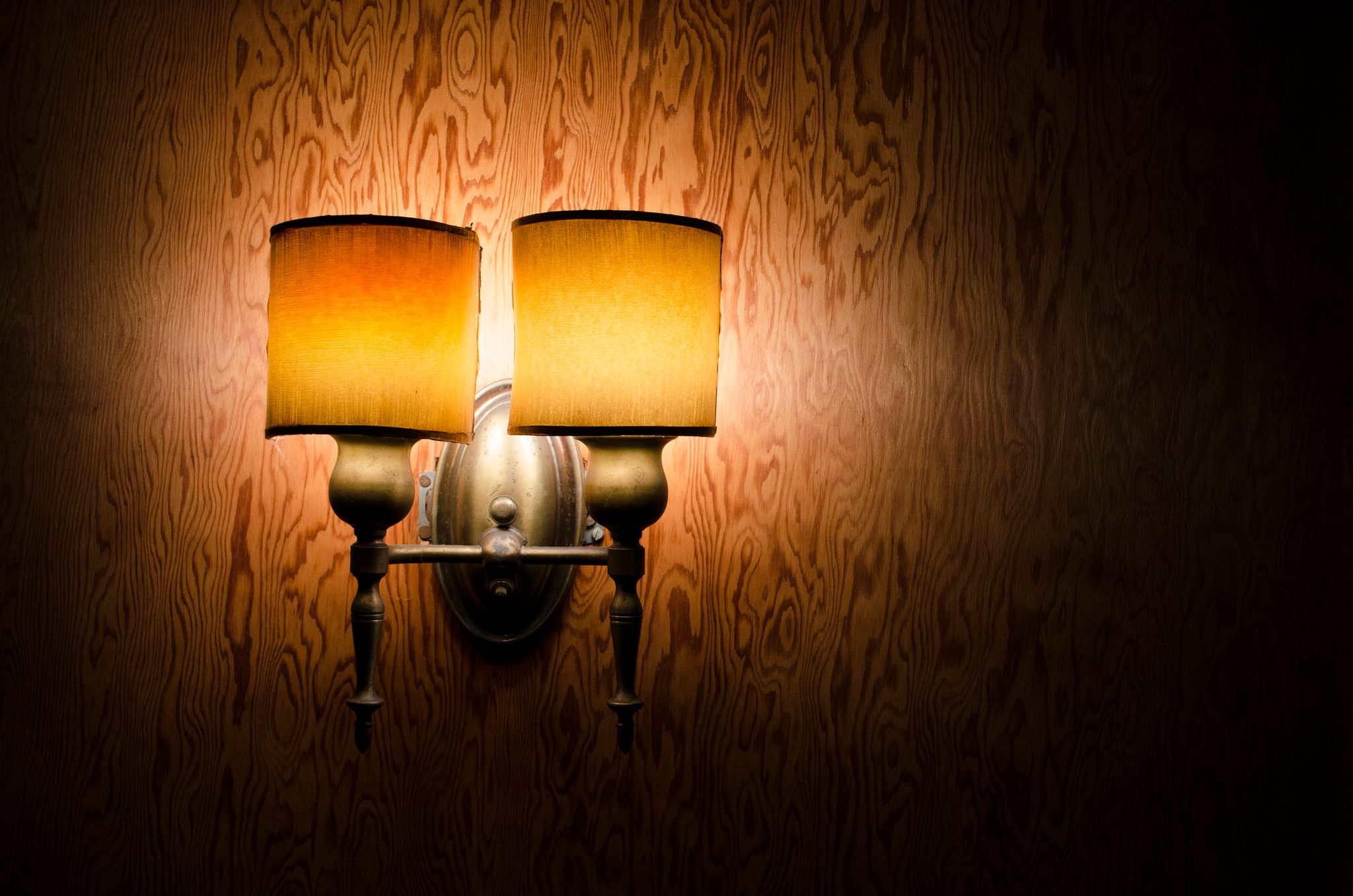 A double sconce glows against a knotty wood wall. There are times that I brood.