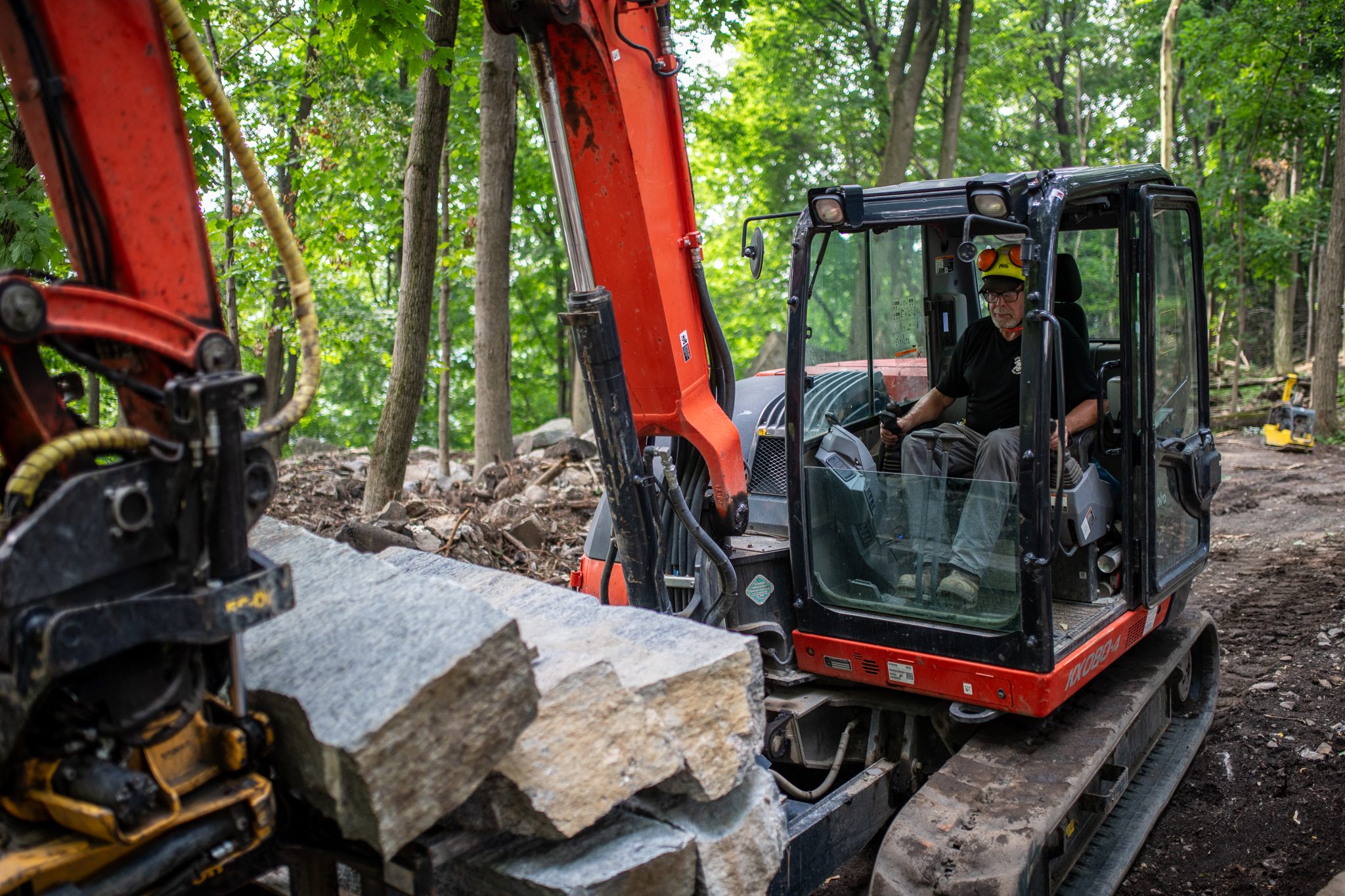 The excavator's grapple holds a granite block while the operator eases it into place.