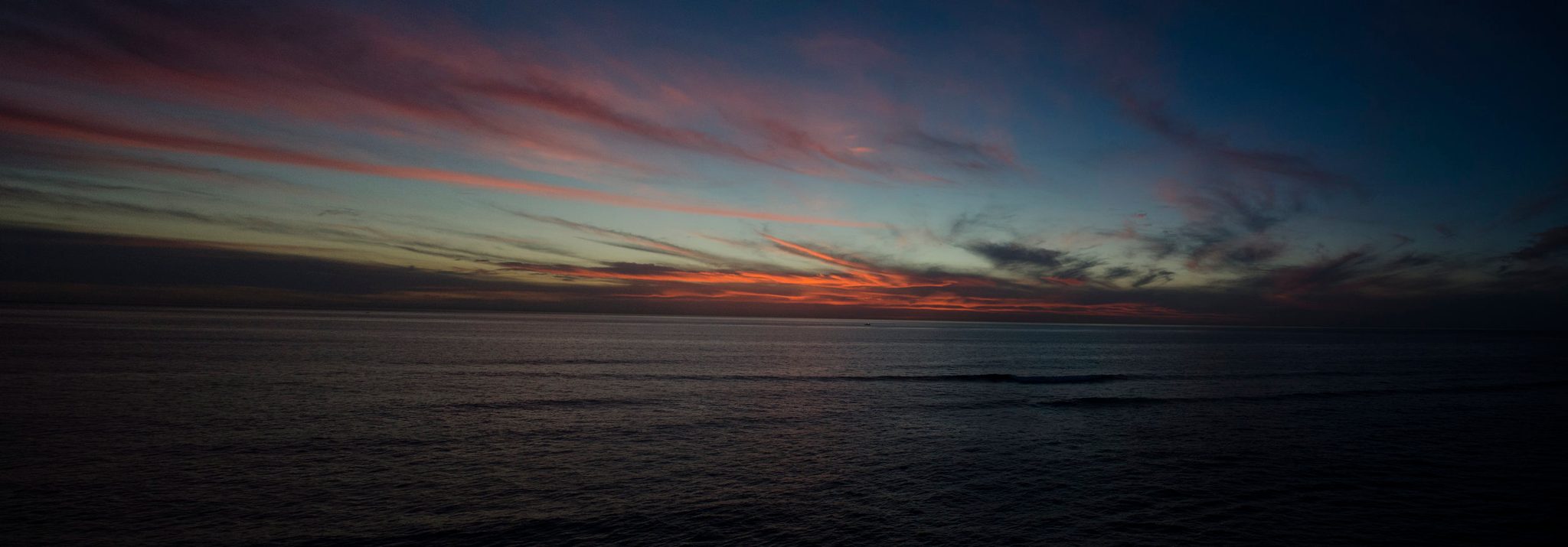 Red streaks of cloud burn over the dark Pacific.