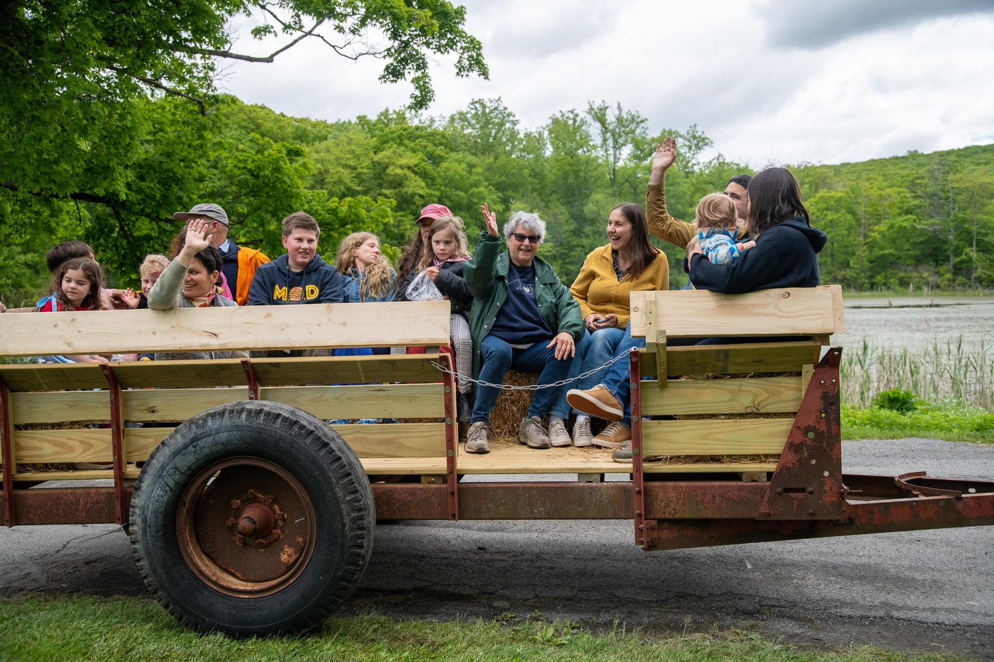 Riders wave from the wagon as it passes the pond.