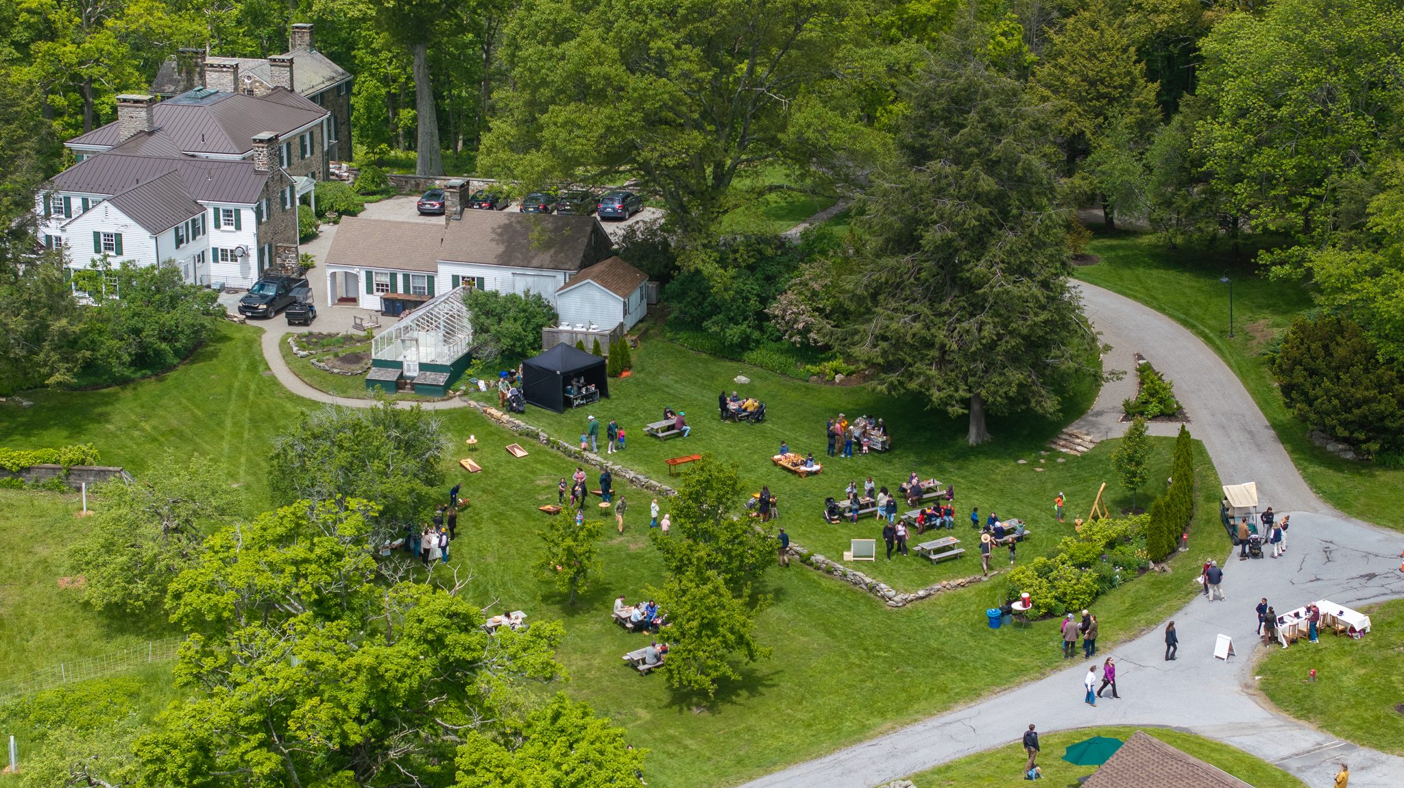 Families gather on the lawn beneath the old farmhouse, the day in full swing.