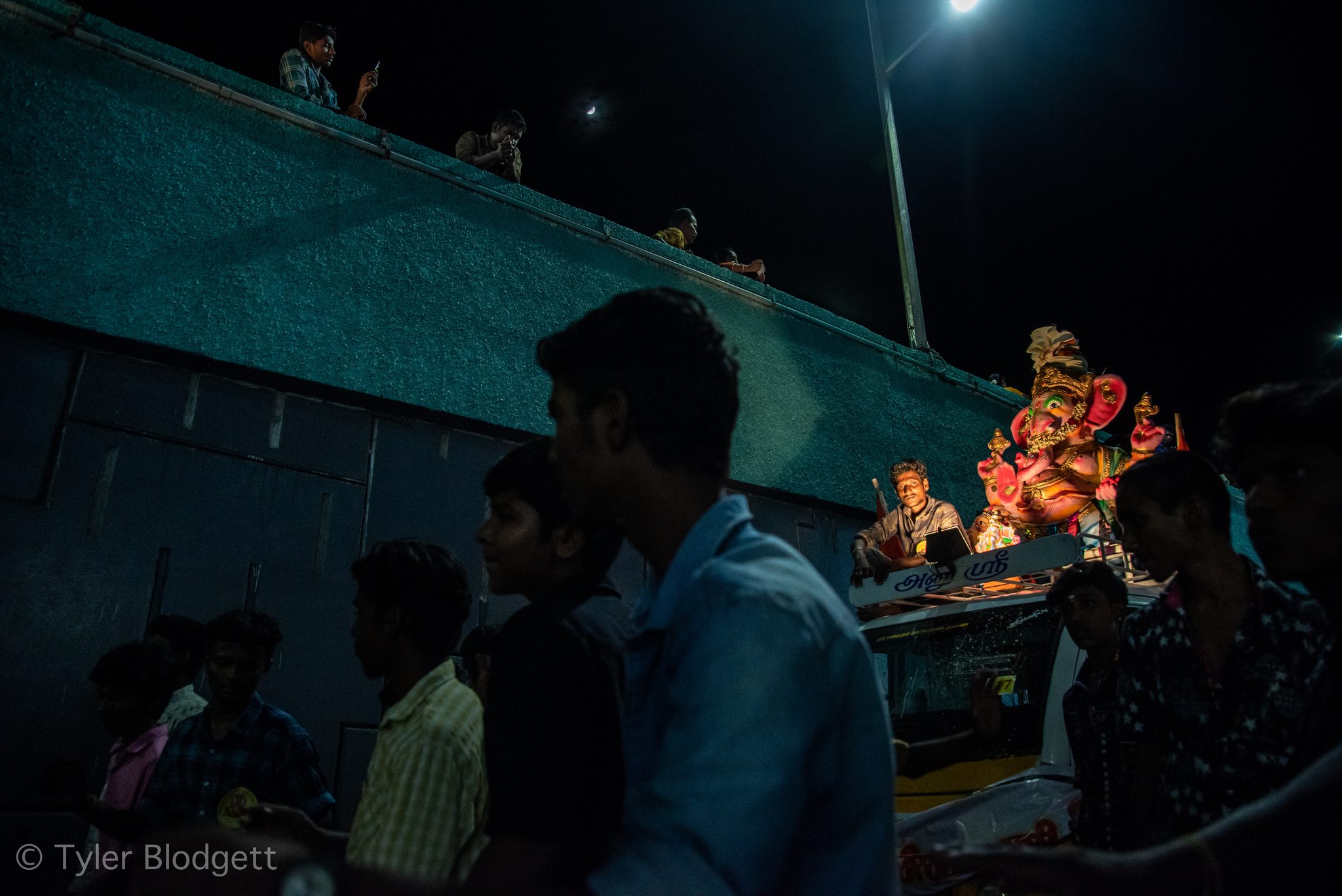 The crowd gathers at night as Ganesha rides past on a lit float.