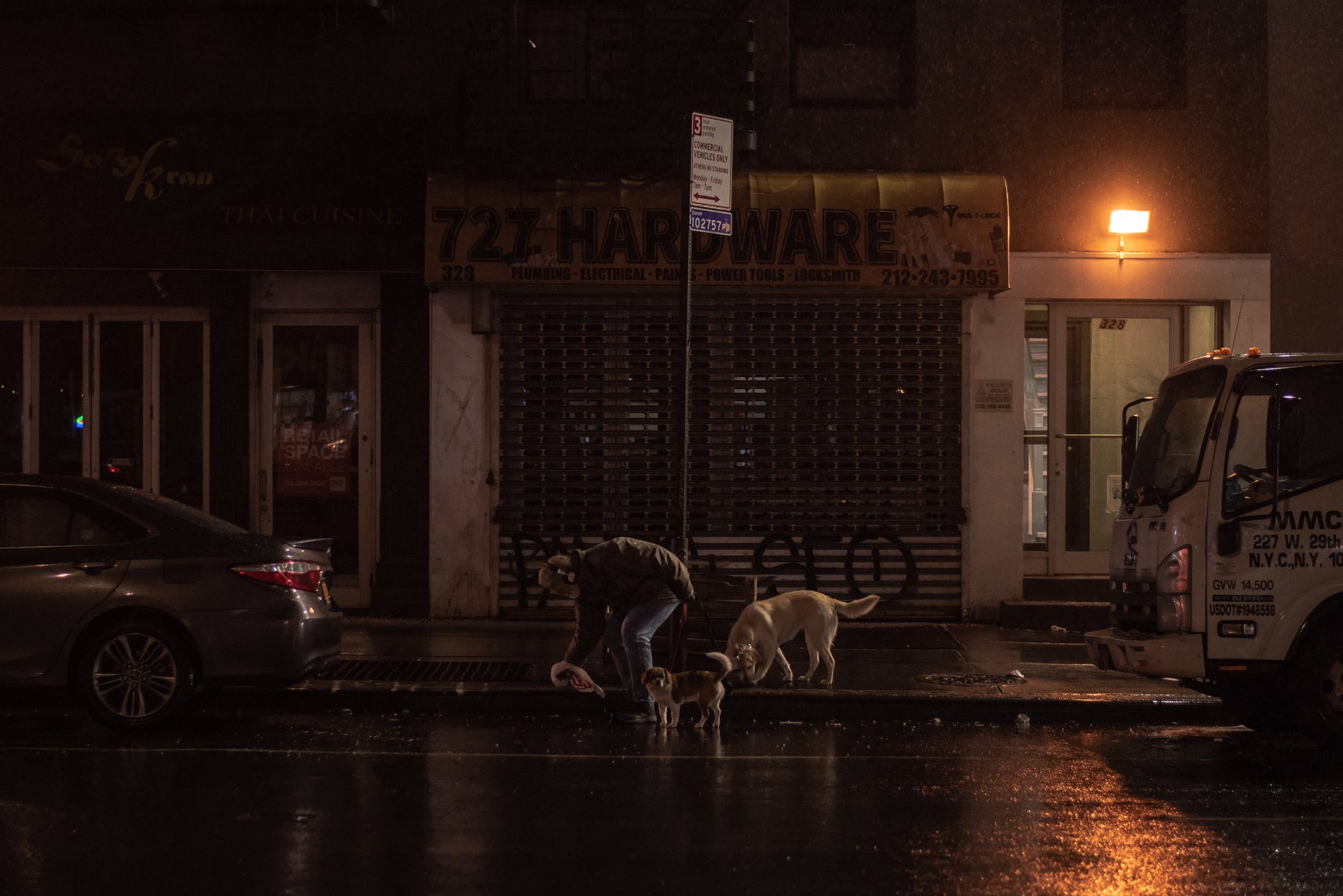 In the rain, a man walks his dogs past the shuttered hardware store.