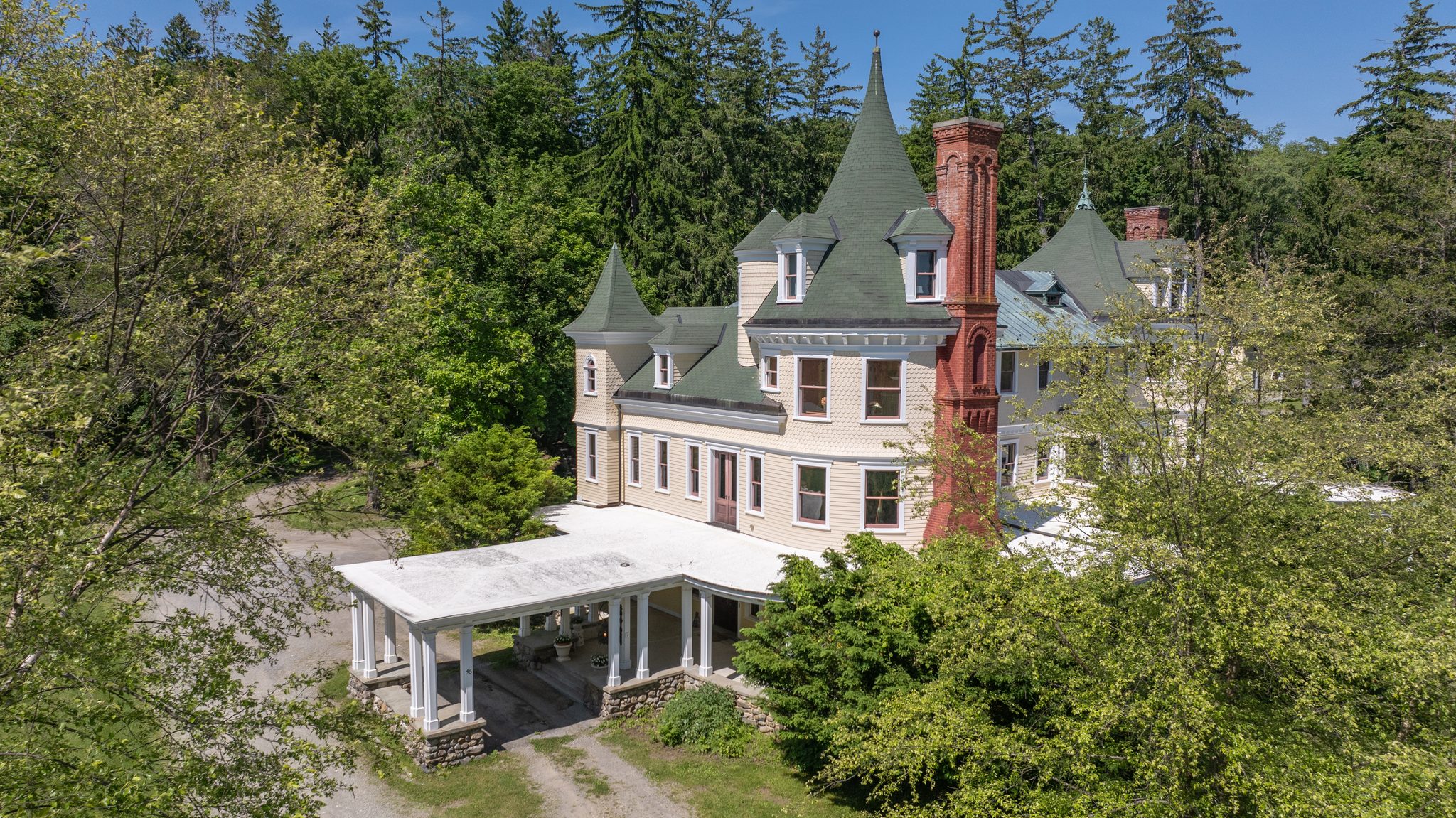 From above, a white porte-cochere reaches out from the side of the house toward the gravel drive.