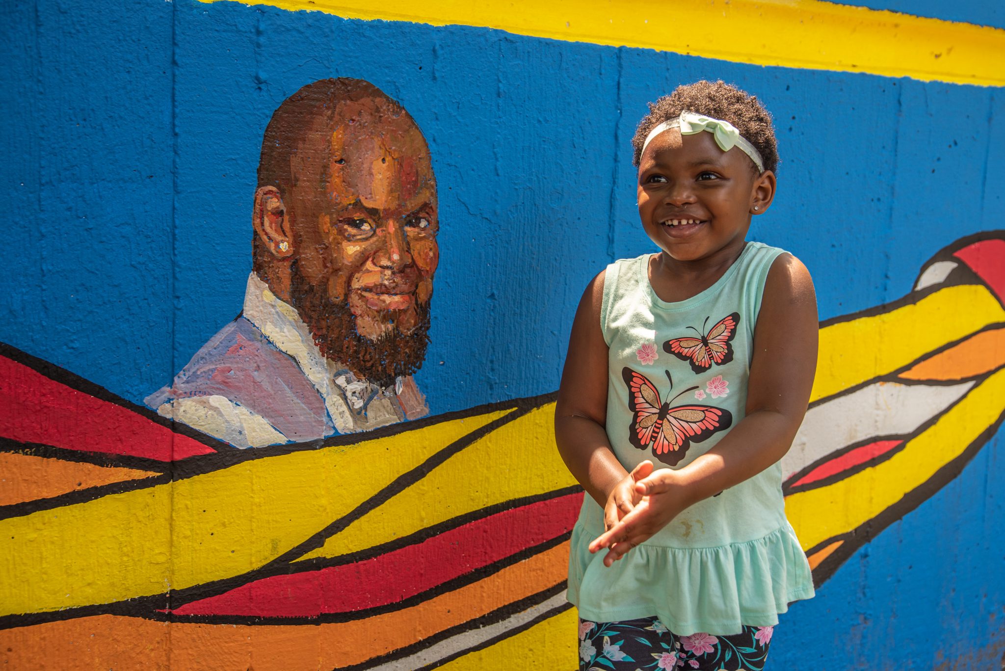 A girl grins beside the painted portrait, a butterfly on her shirt.