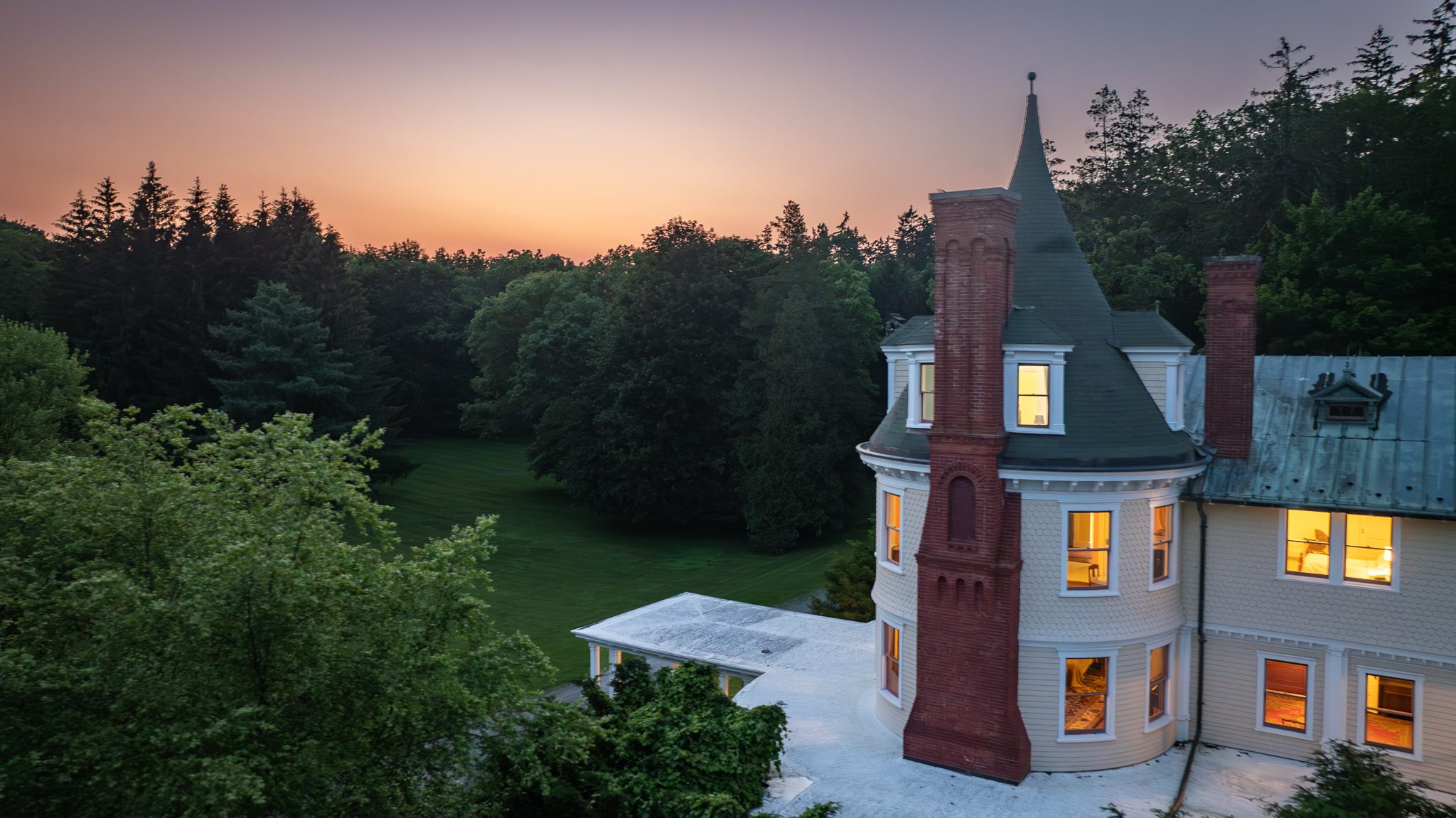 The turret and red brick chimney in the last of the afterglow, warm windows stacked one above another.