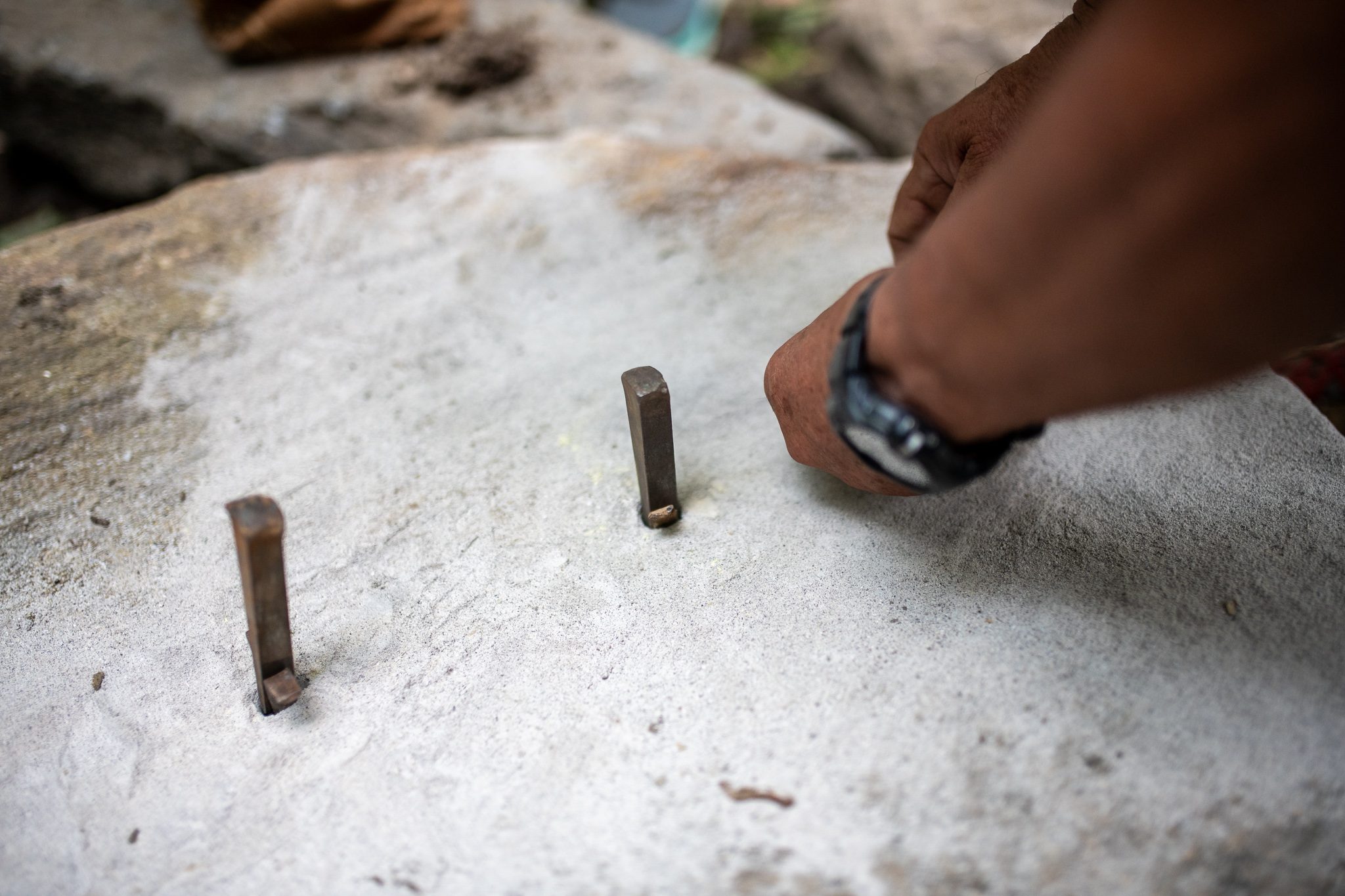 Steel wedges stand in a row of drilled holes, waiting for the hammer.