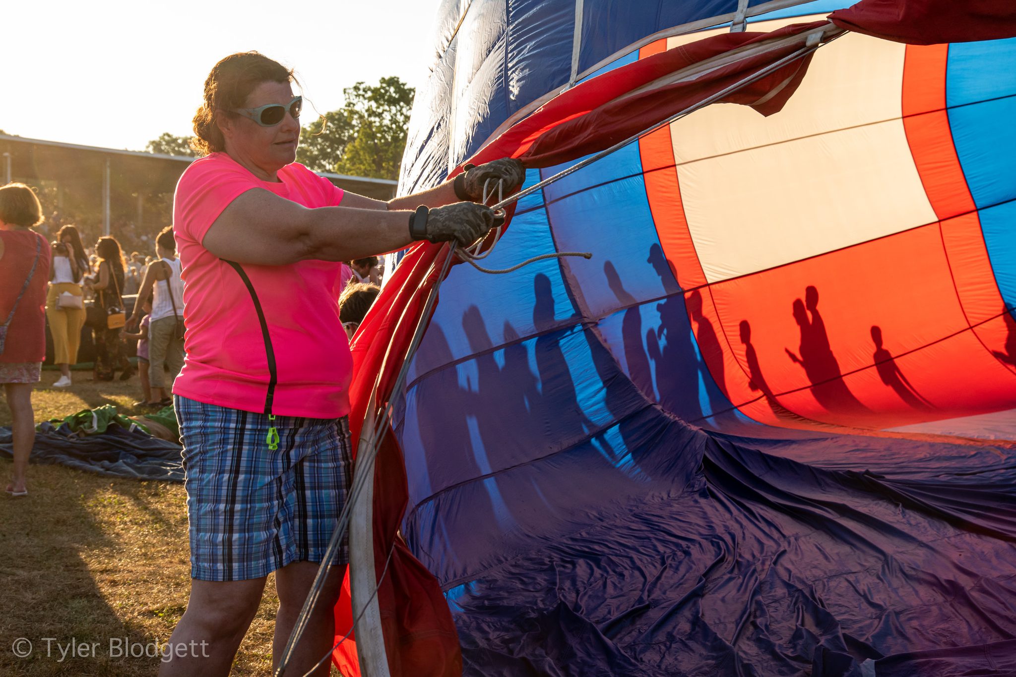 A woman steadies the envelope while the crowd's shadows fall across the fabric.