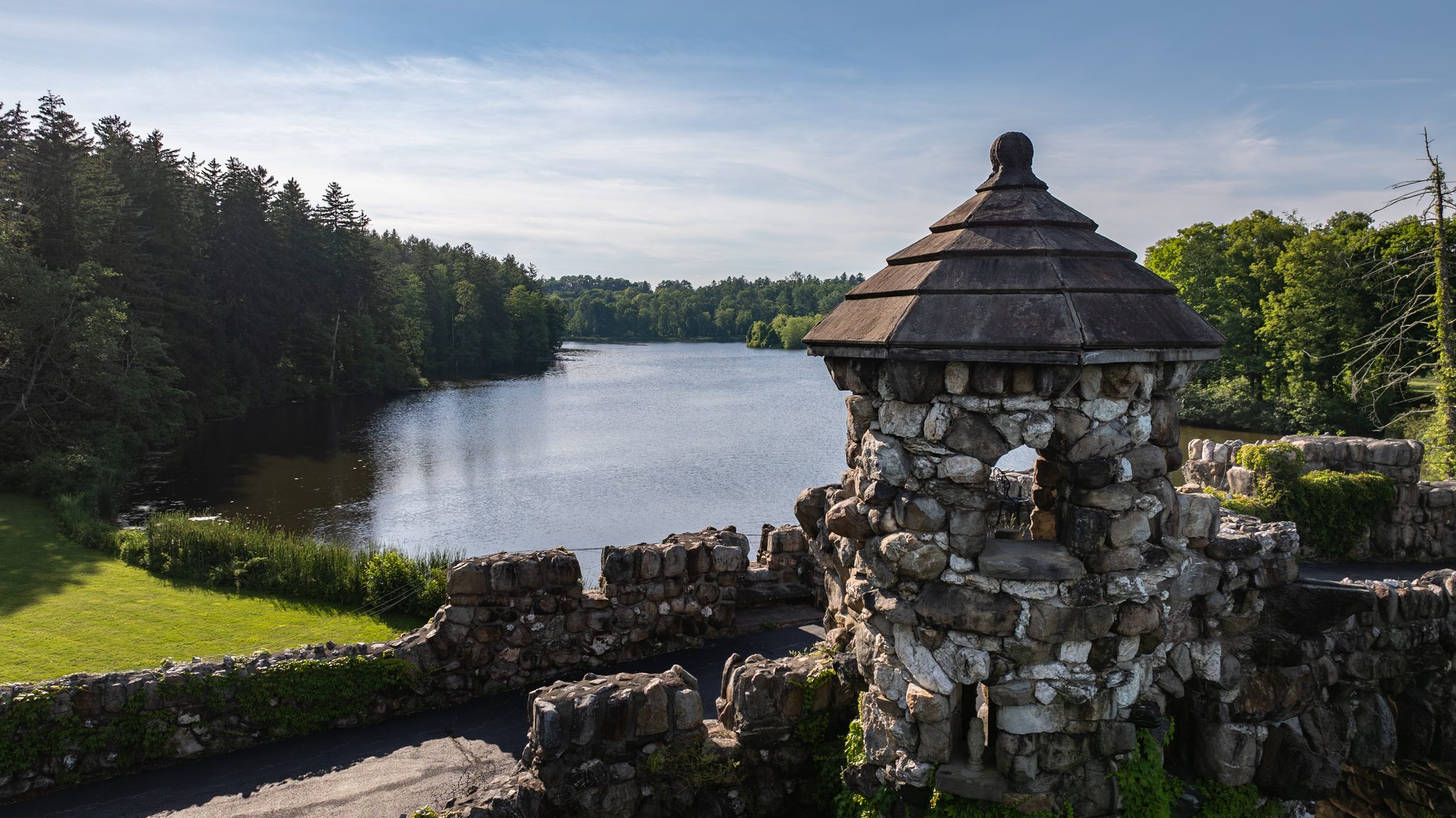 The stone turret on the lake bridge up close, its shingled cap against a pale July sky and dark pines.