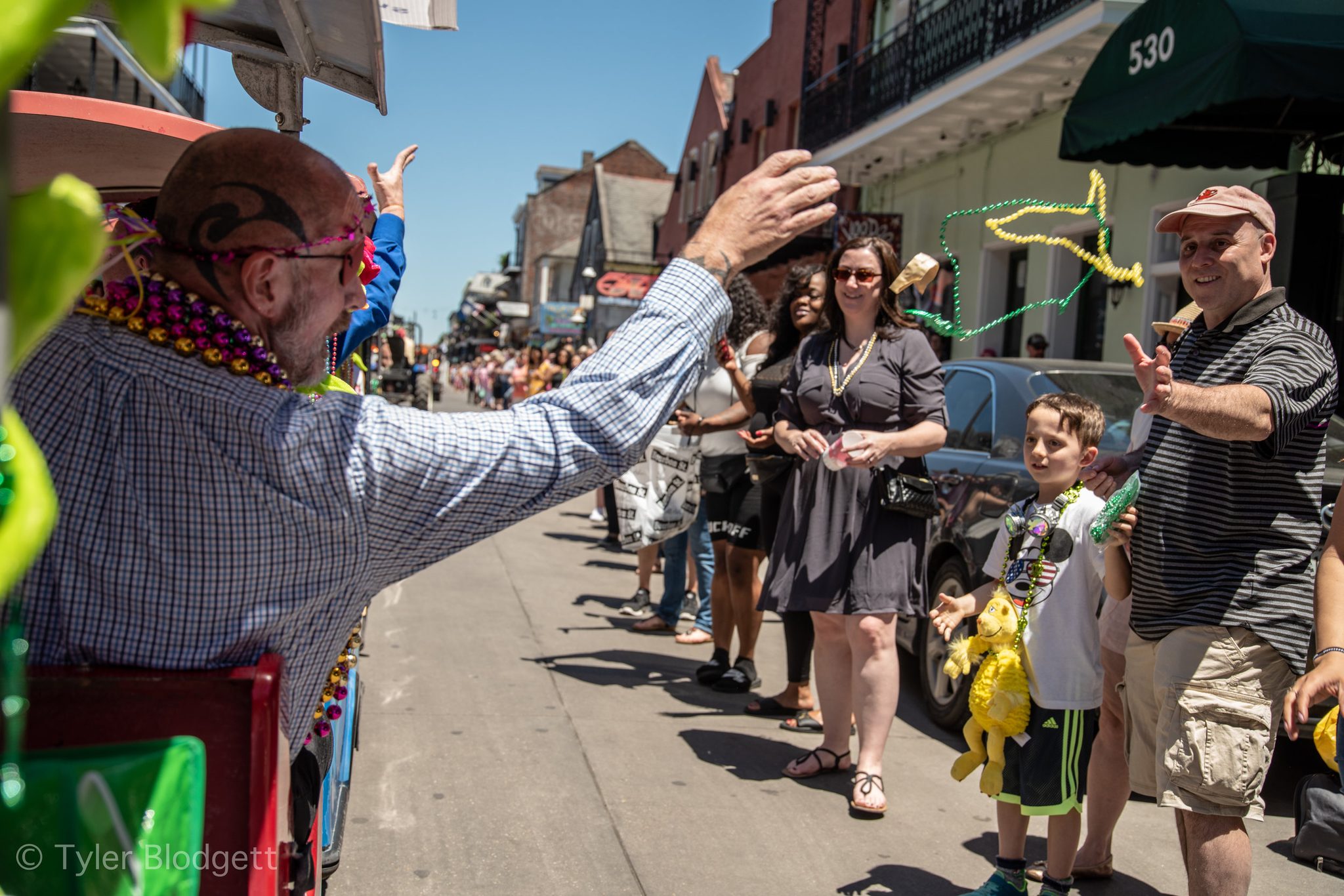 A rider leans from his float toward the sidewalk, where every hand is up and every neck is heavy with beads.