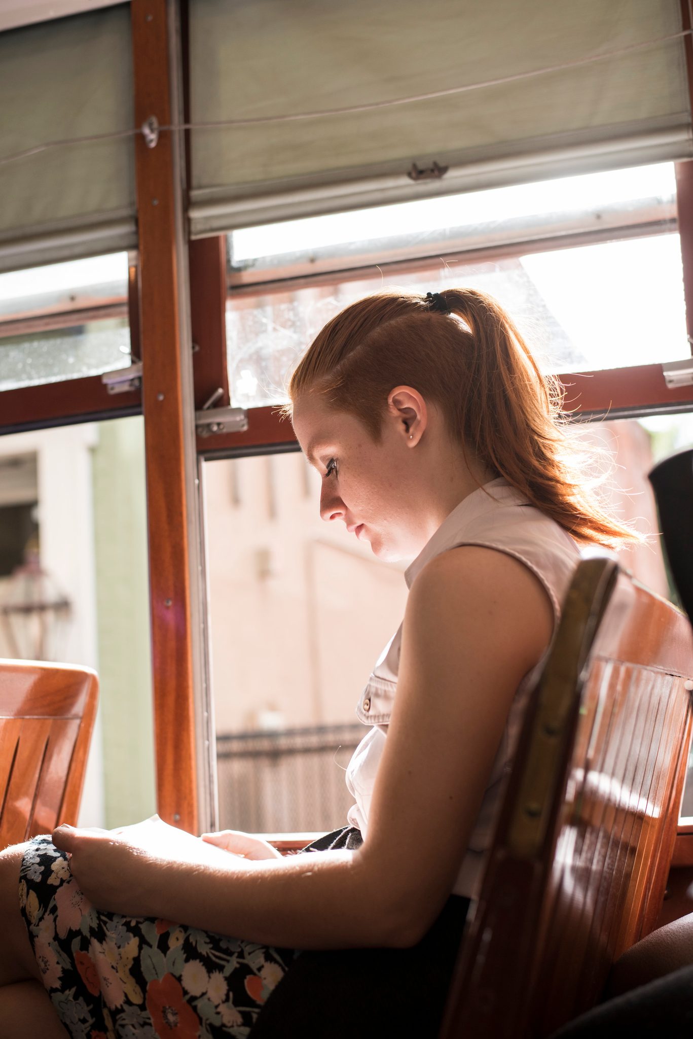 A young woman reads by the streetcar window, the light falling across her page.