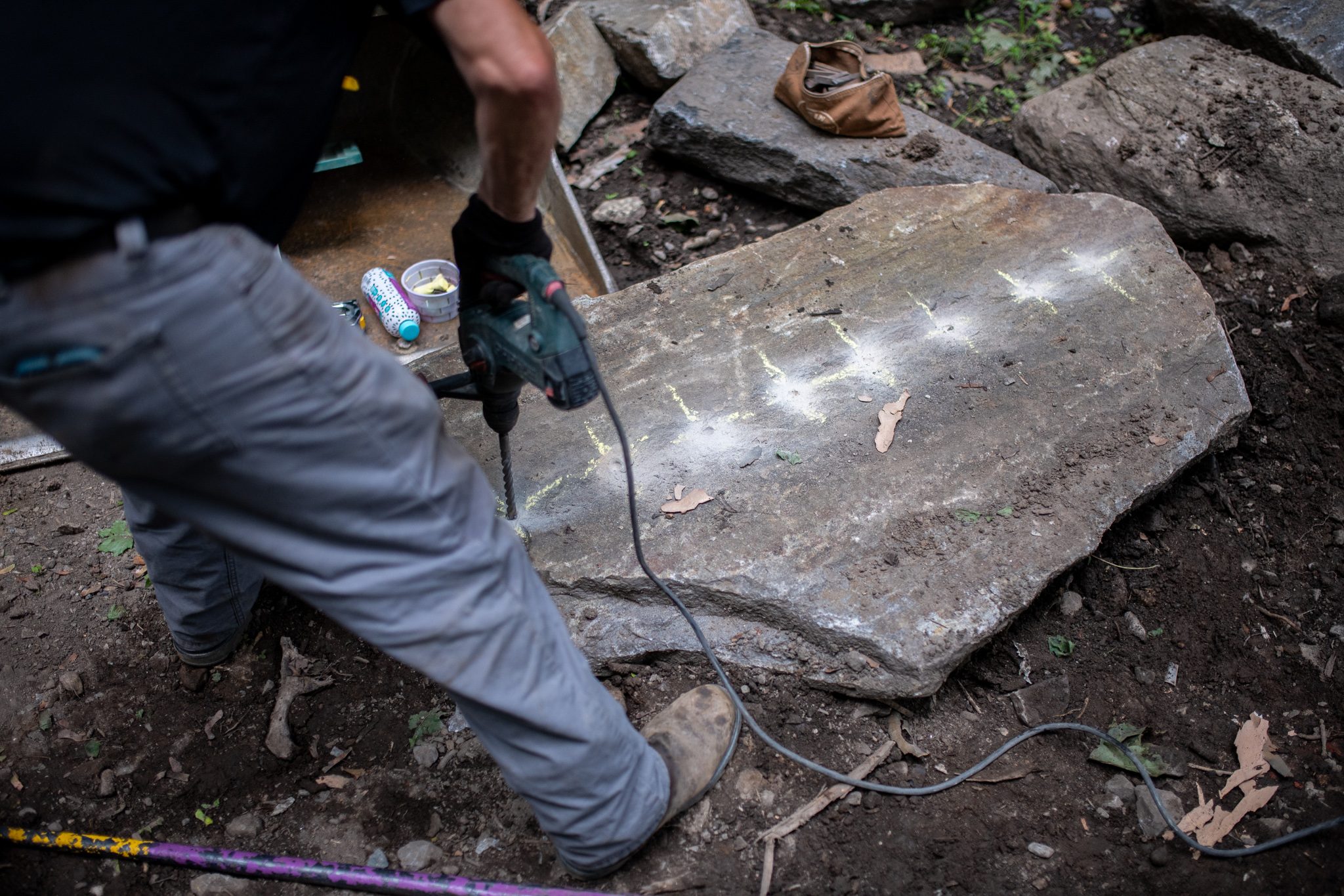 A drill bores a row of holes along a chalk line in the stone.