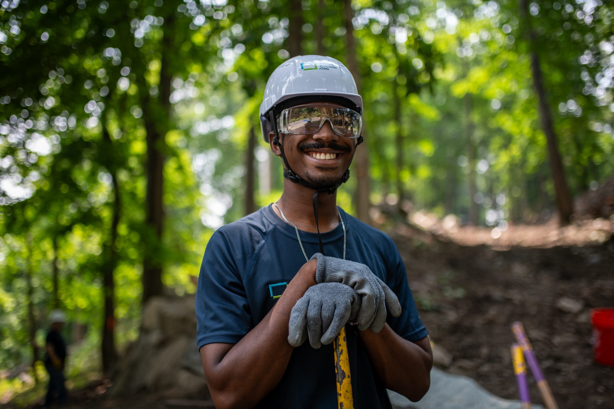 A crew member leans on his tool, grinning under his helmet.