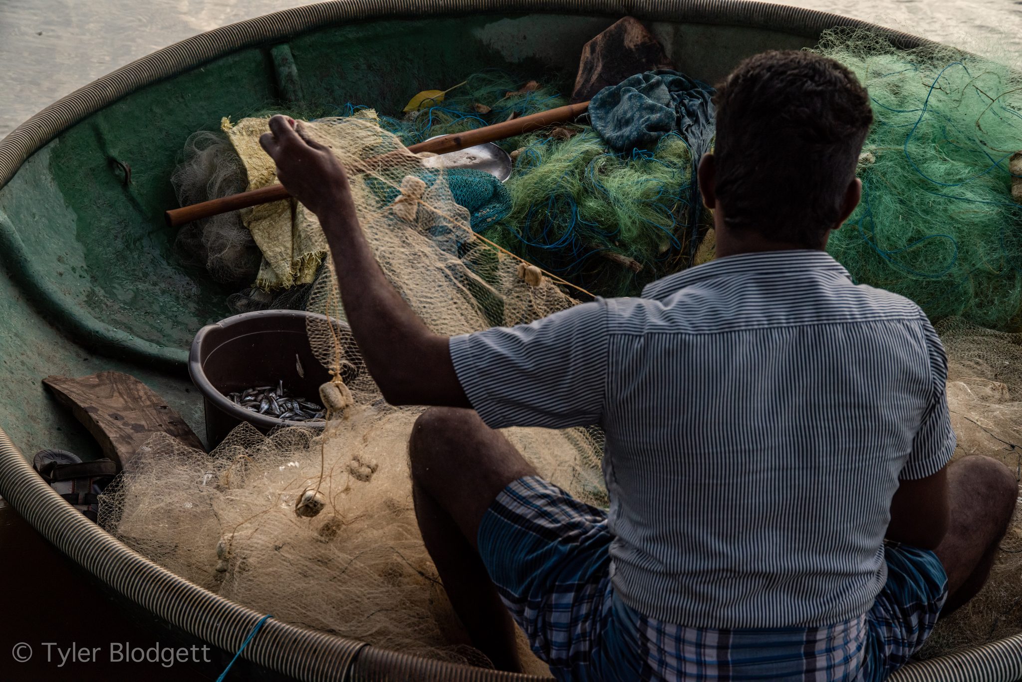 A fisherman untangles his net in a round coracle.