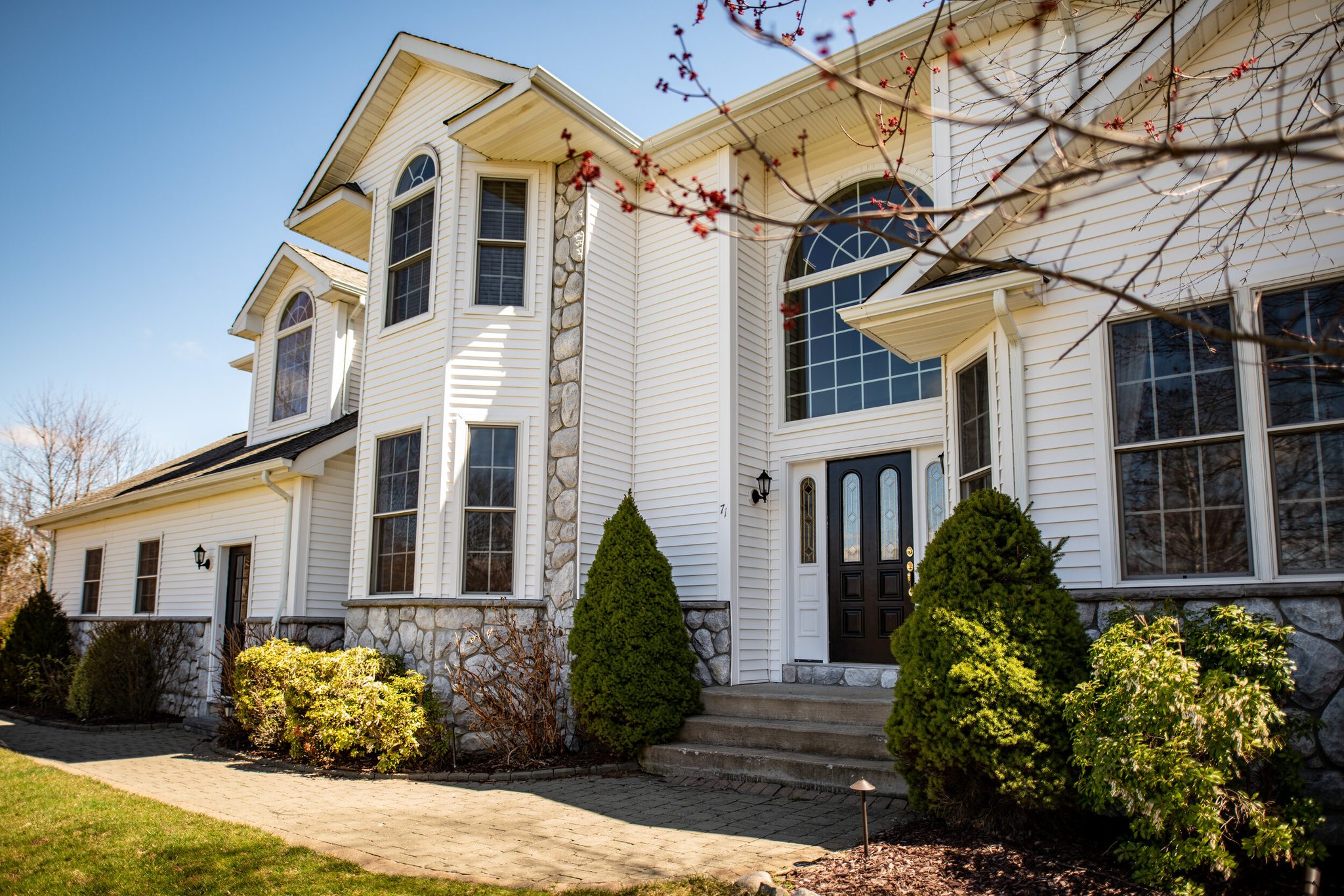 Stone and white clapboard rise to a tall arched window above the front door.