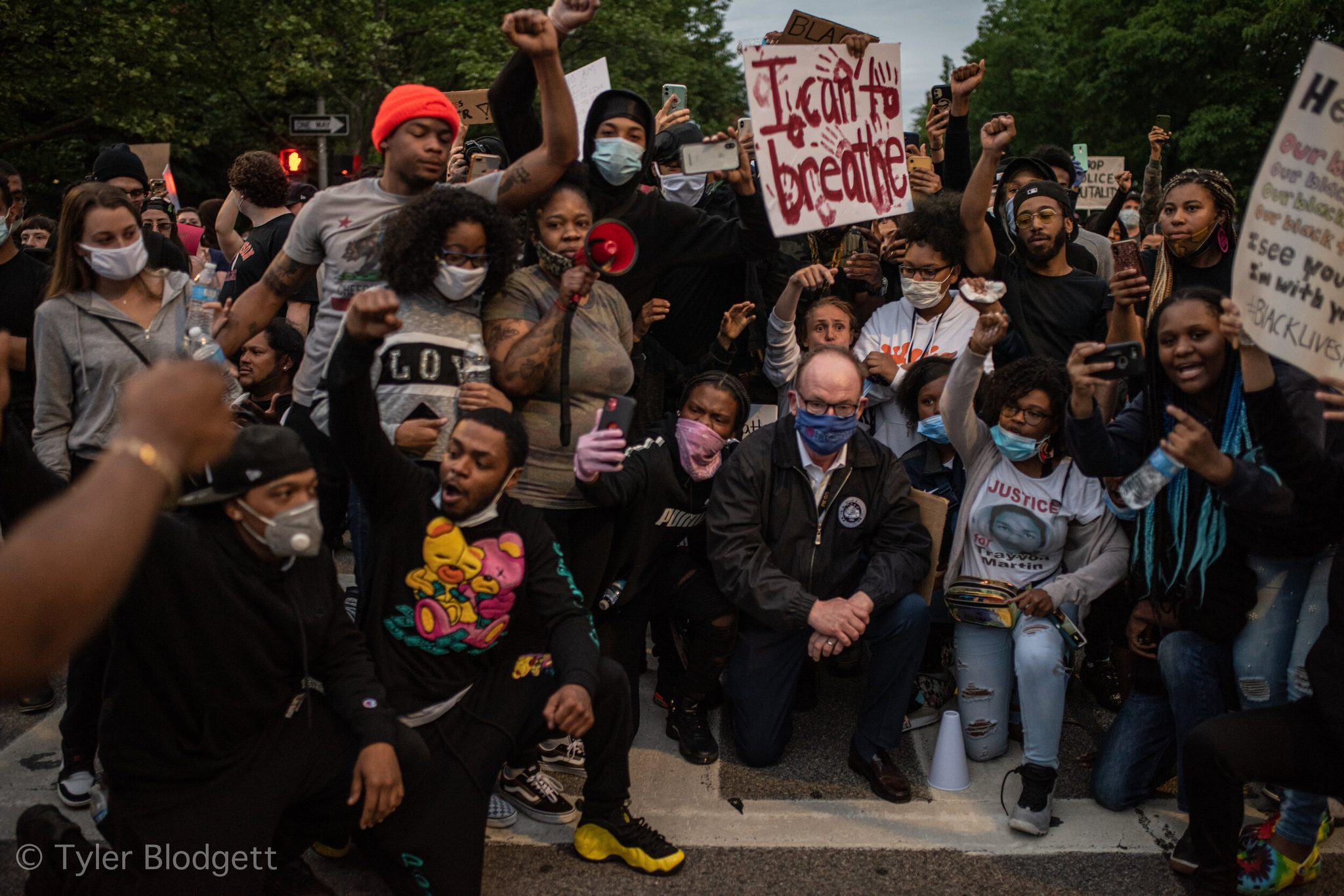 The crowd takes a knee with fists raised, an I Can't Breathe sign held high above them.