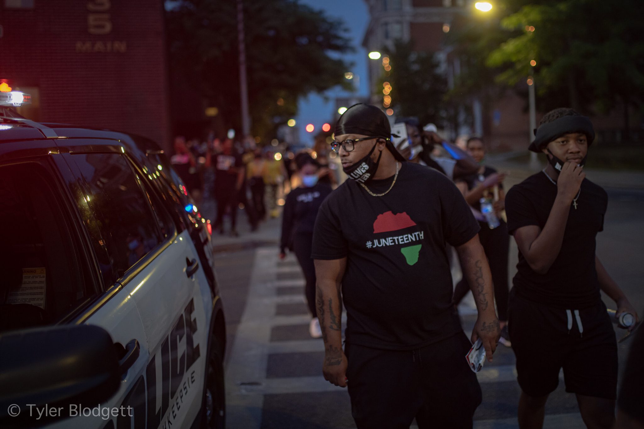 A marcher in a Juneteenth shirt walks past a police SUV, and the whole street follows.