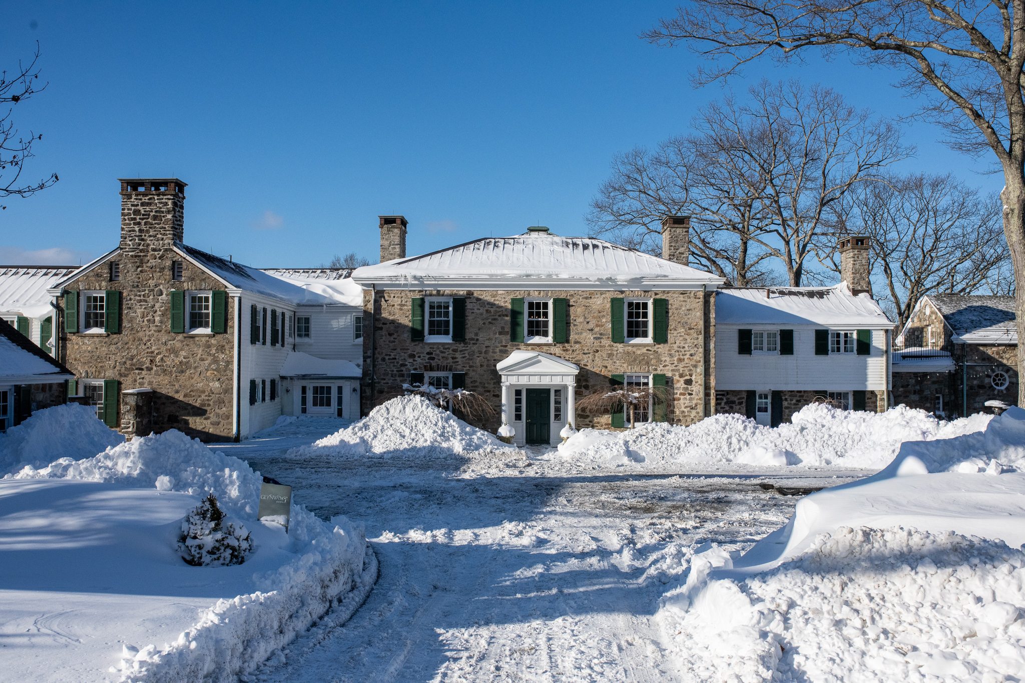 The fieldstone manor after the storm, paths dug out through waist-high snow.