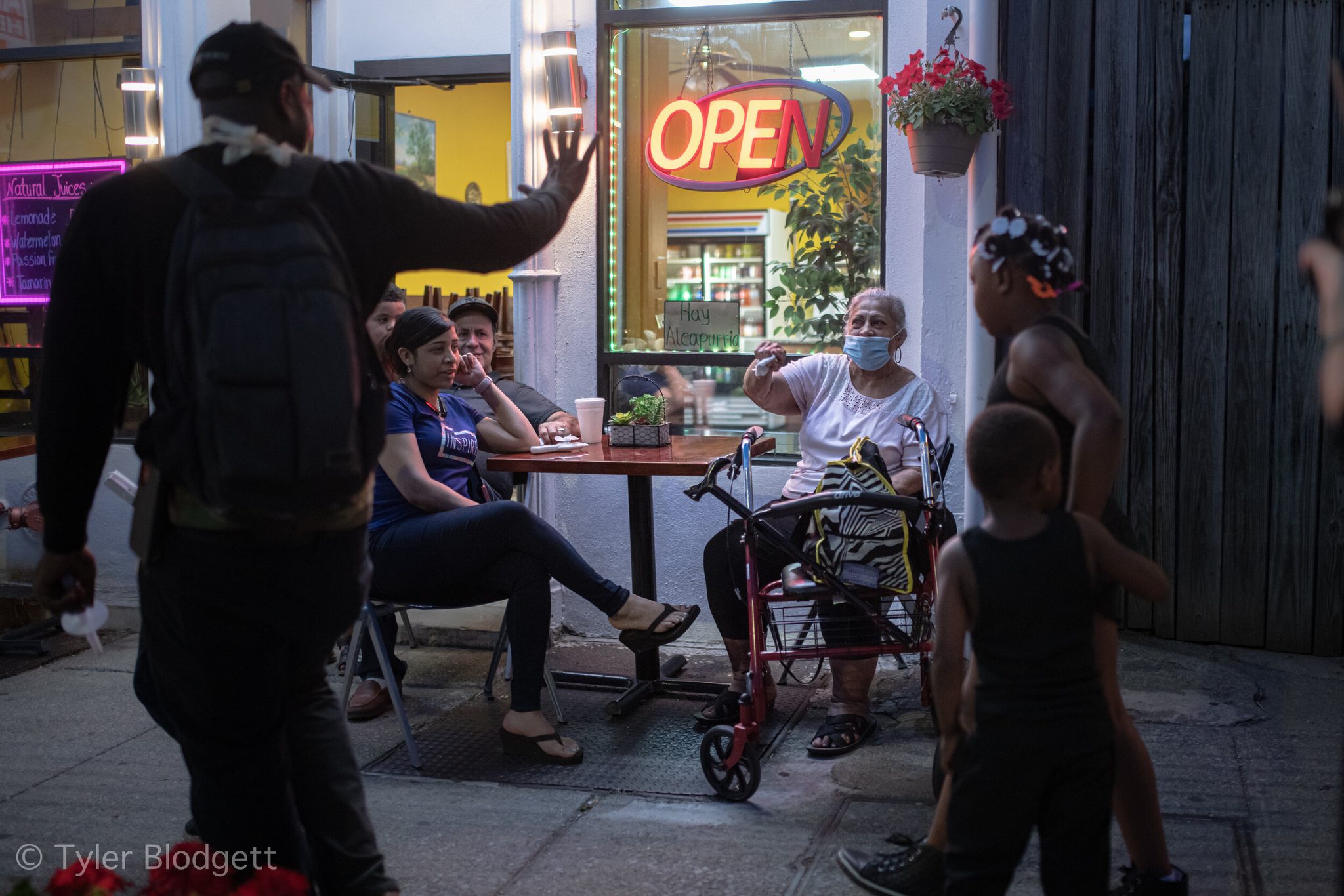 A marcher waves to the cafe table as he passes, and the woman with the walker waves right back.