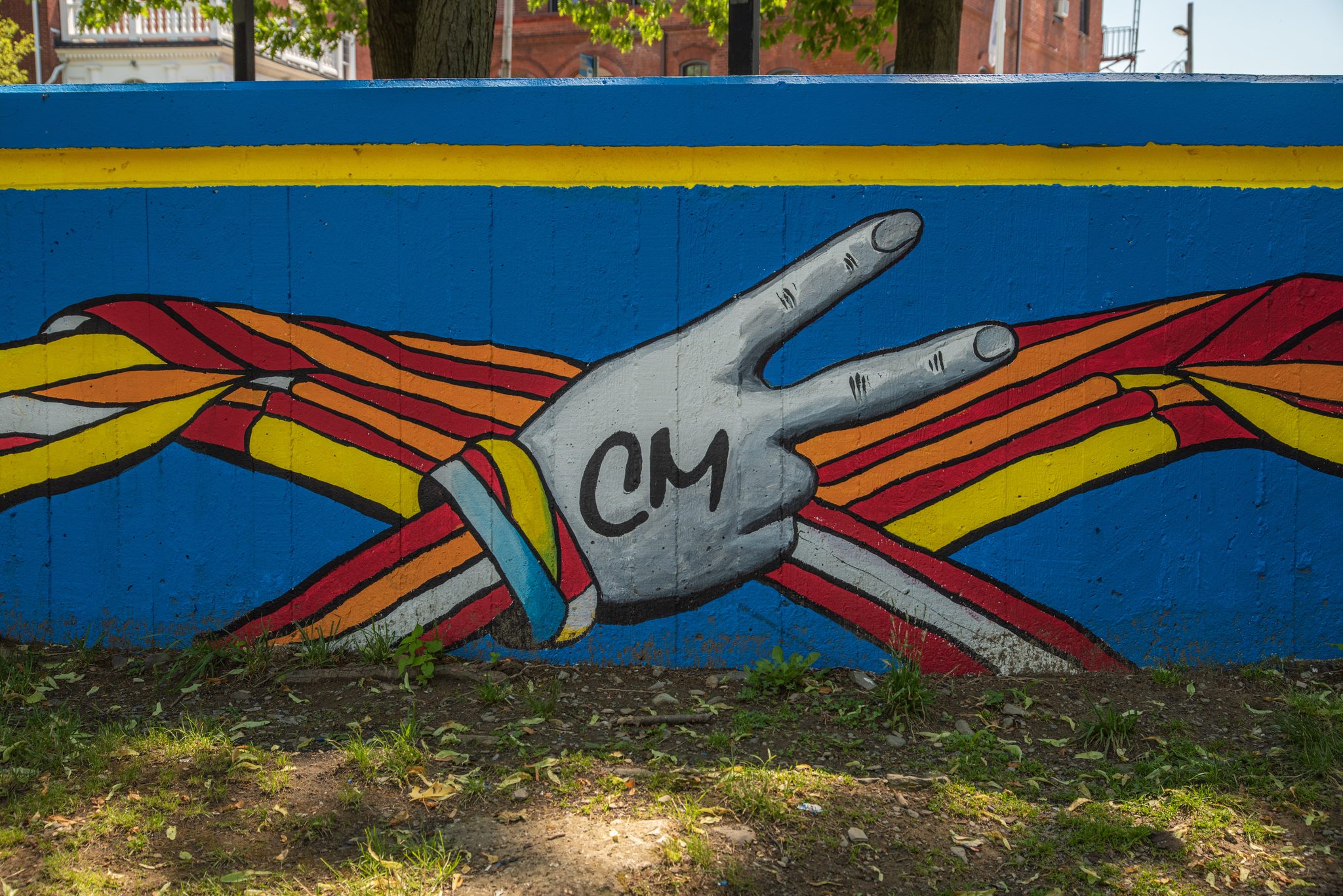 A painted hand throws up the CM sign, wrapped in ribbons of the same colors.