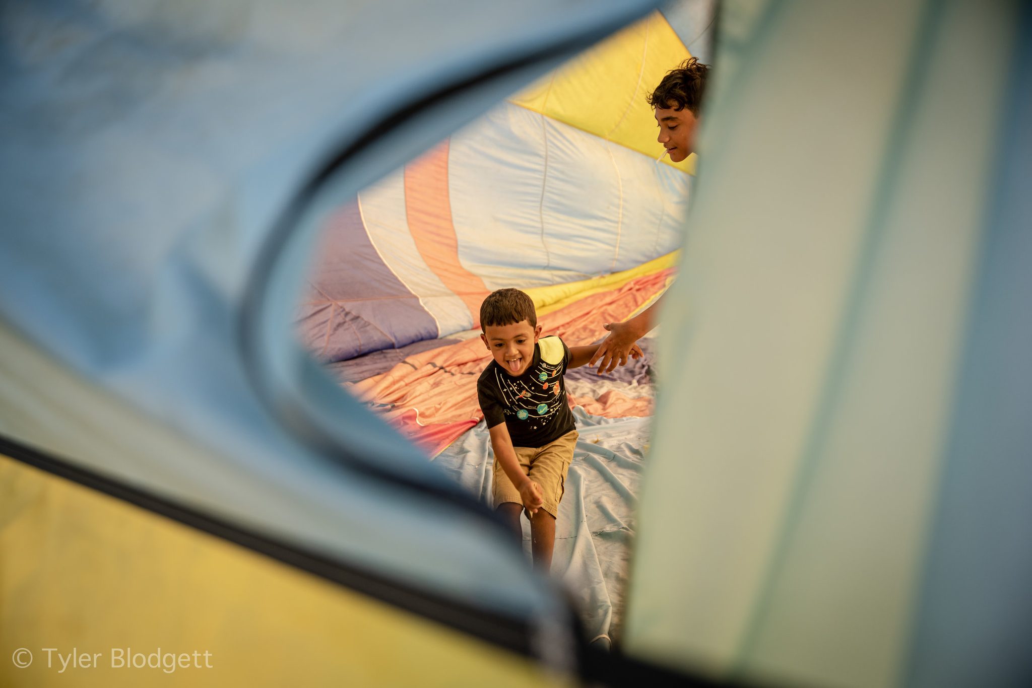 A boy slips out from inside a balloon still swelling with cold air. Before the burners roar, the envelope is a room a child can walk through.