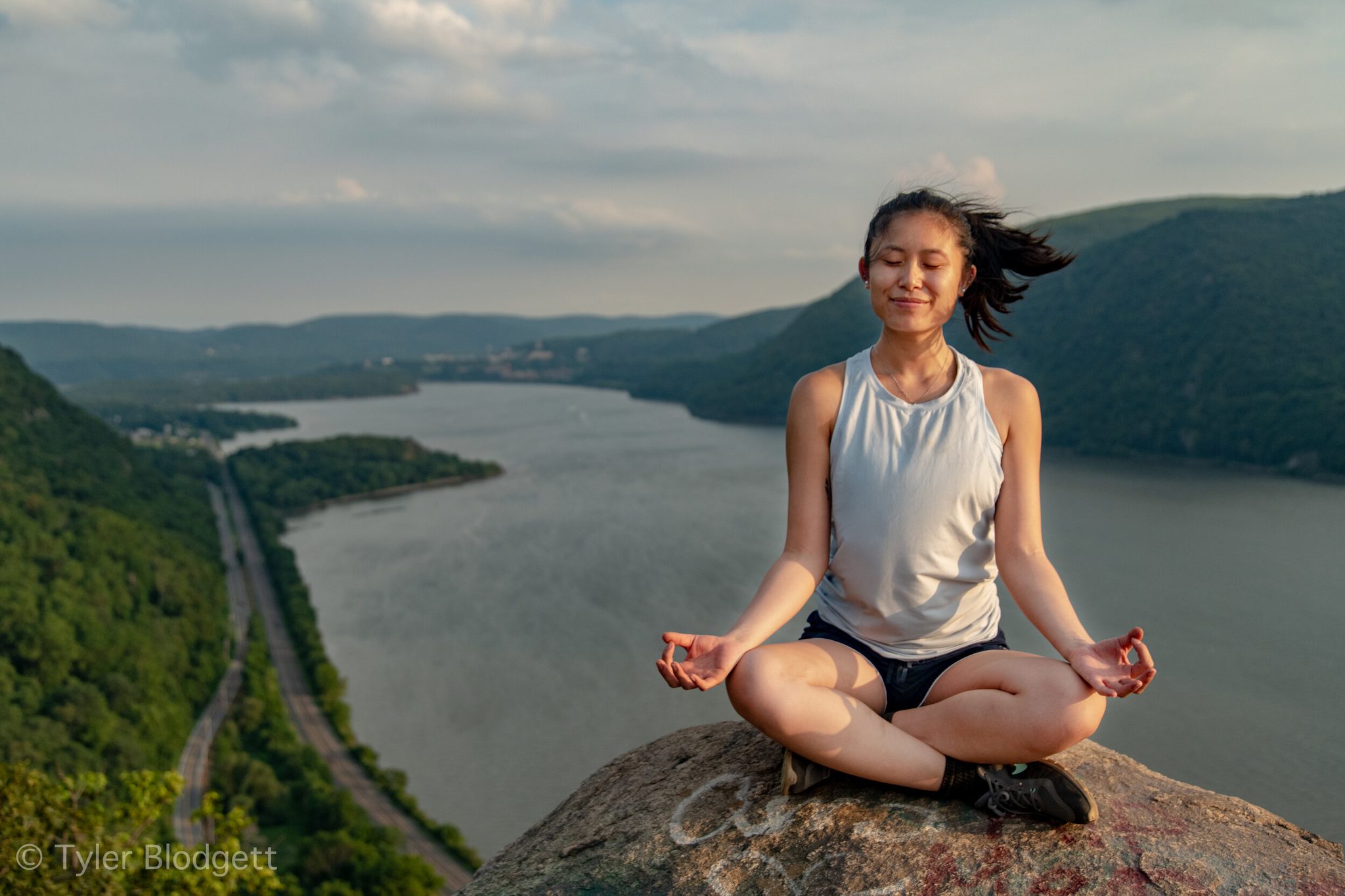 Eyes closed, legs crossed, she meditates on the rock while the Hudson winds away below her.