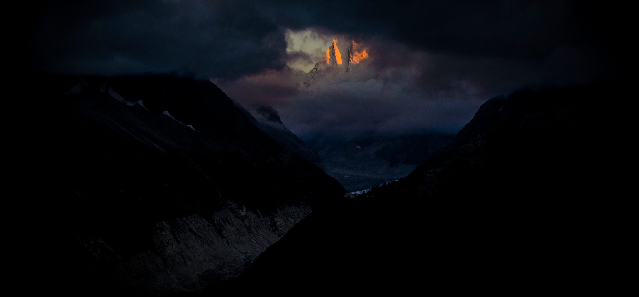 One summit burns through the storm clouds as darkness takes the valley. The emblazoned summit at night.