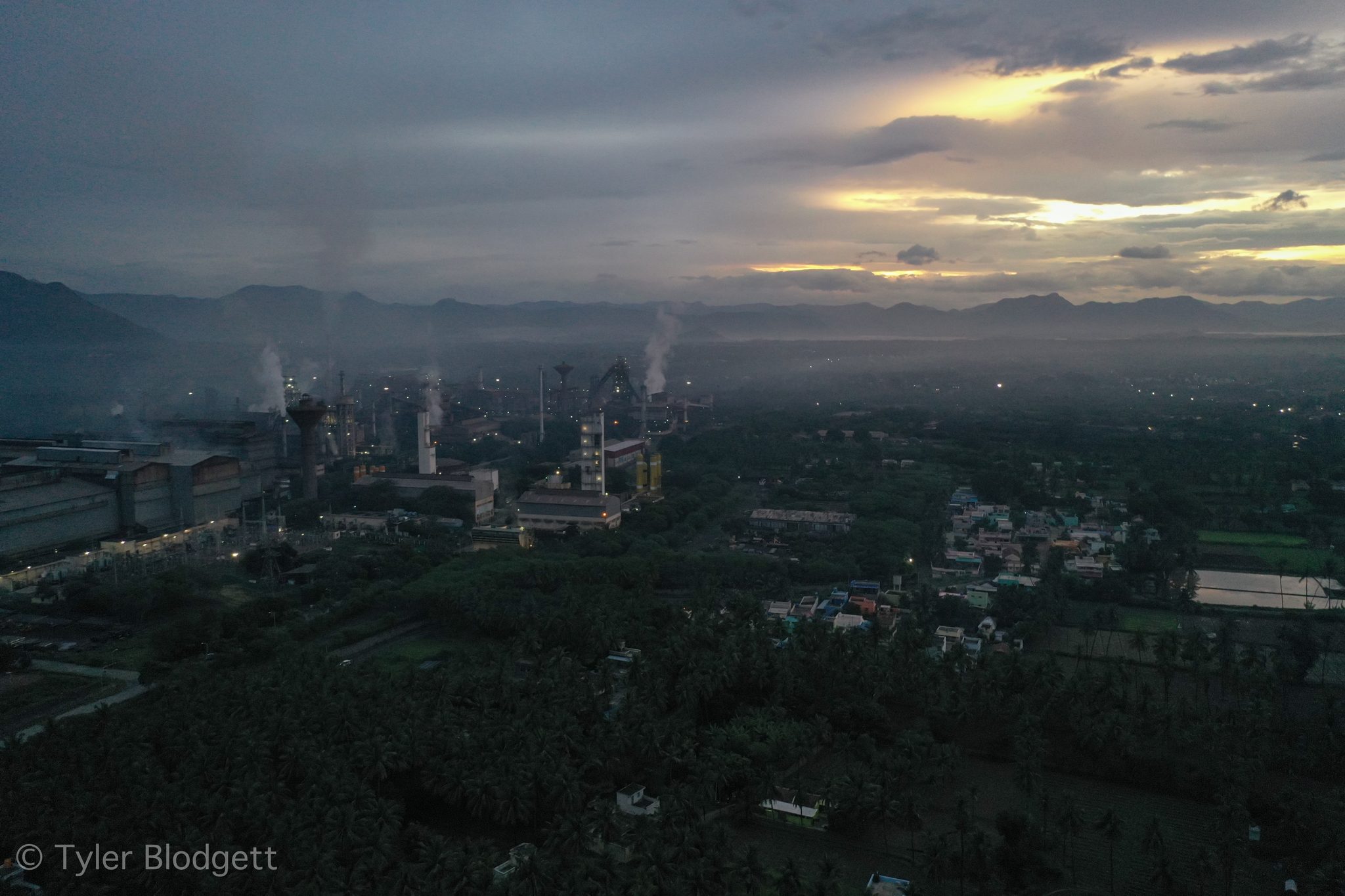 Steam drifts from the factory while the town wakes beneath low clouds.