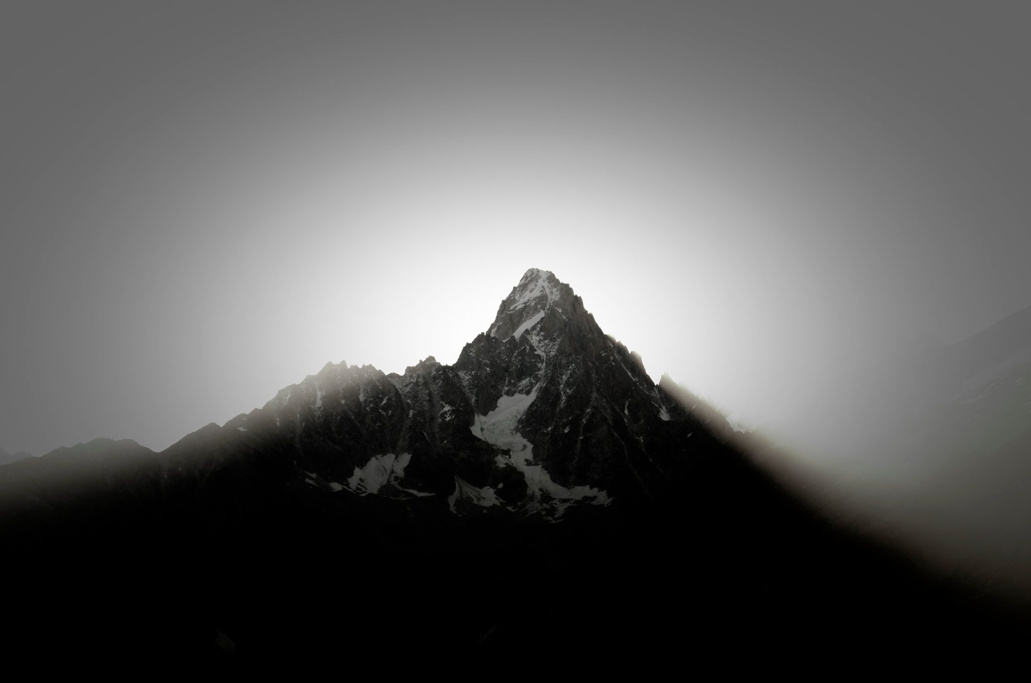 Sunrise breaks behind a lone summit in the French Alps, the light arriving long before the color.