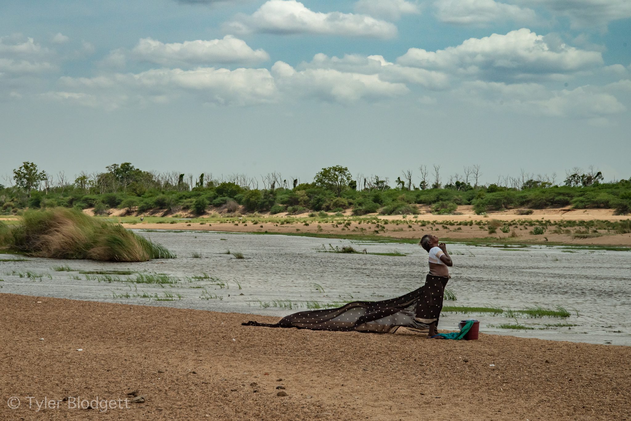 A woman spreads a long cloth to dry on the riverbank.