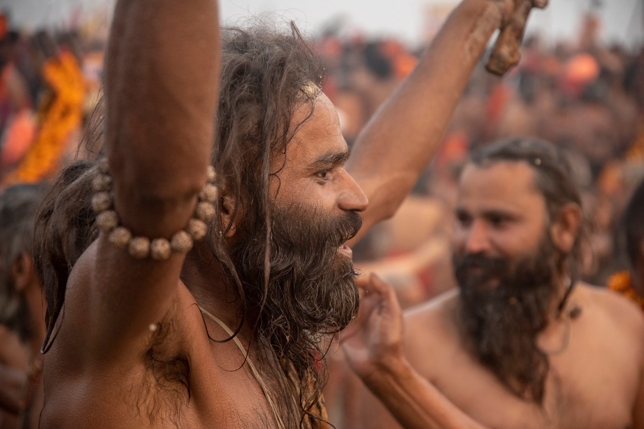 A sadhu throws his head back mid-chant, prayer beads wrapped around his raised arm.